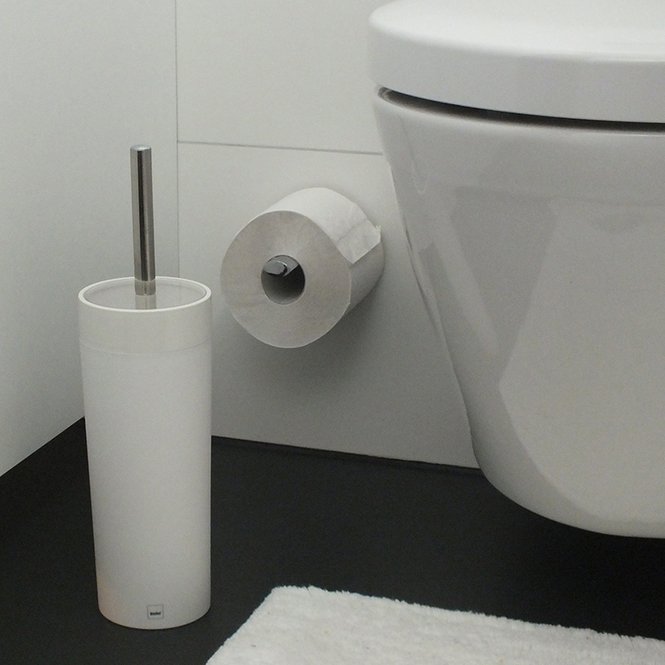 Toilette mit montierter Toilettenpapierrolle und WC-Bürste im Halter daneben, frontal aufgenommen.