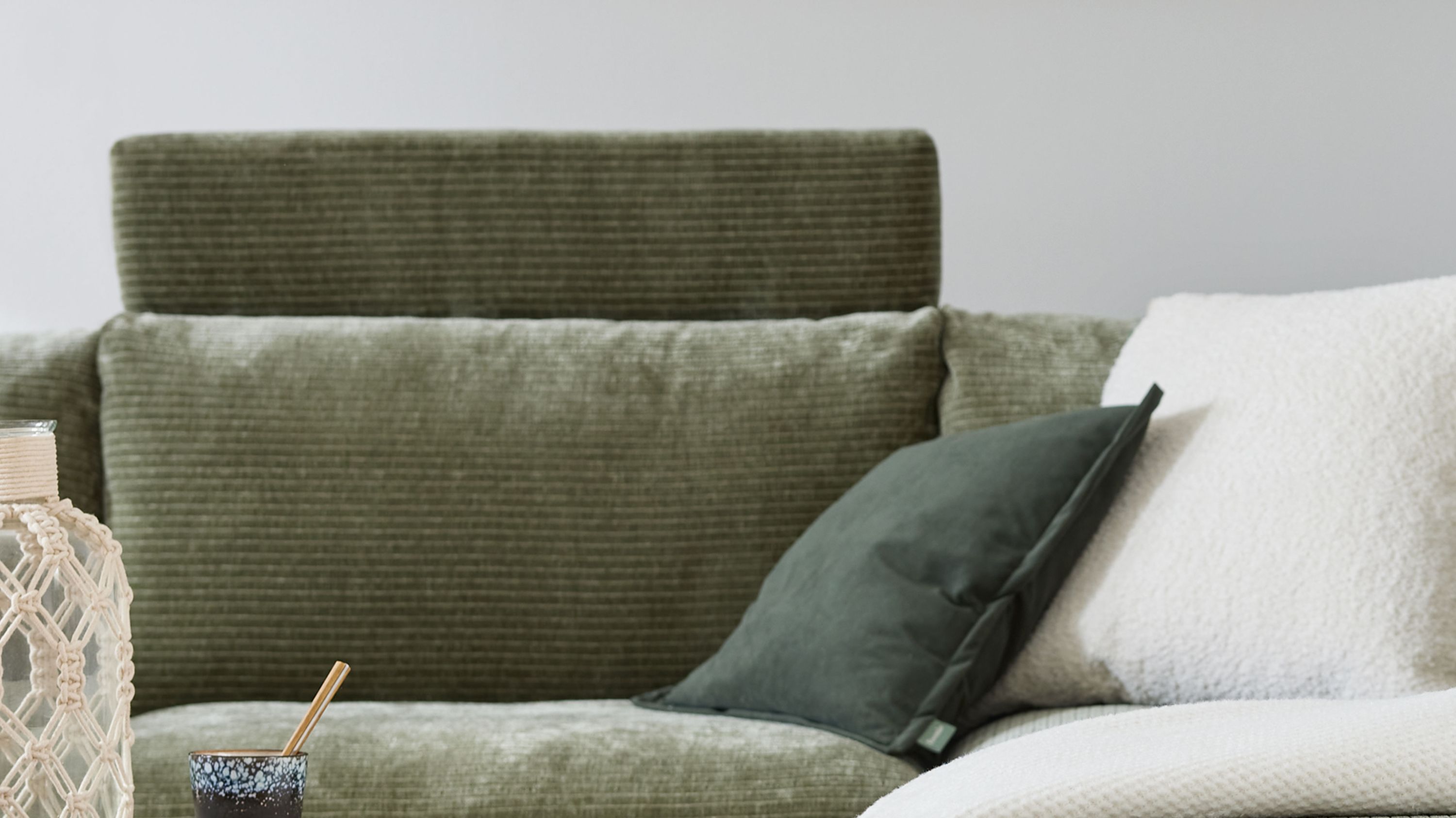 Sofa mit rechteckiger Kopfstütze in grünlichem Bezug und zwei Kissen in dunkelgrün und weiß