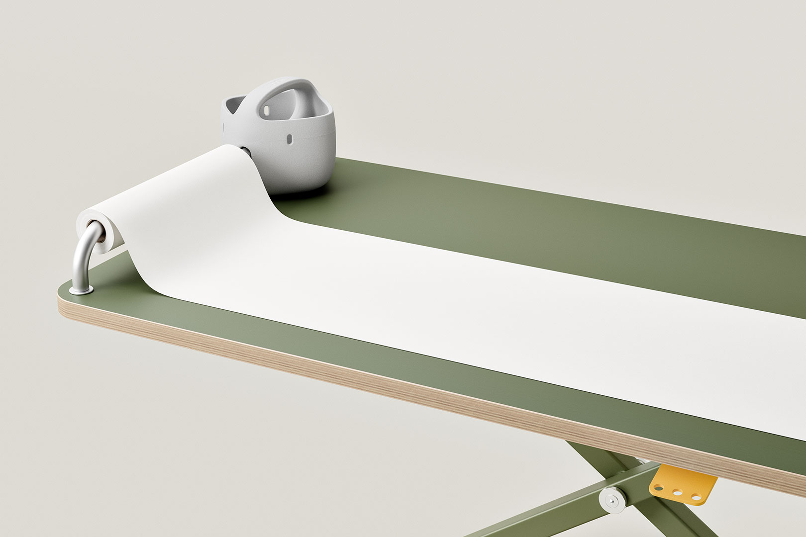 Papierrolle auf Metallstange an grünem Schreibtisch befestigt, grauer Halter als funktionales Schreibtischzubehör