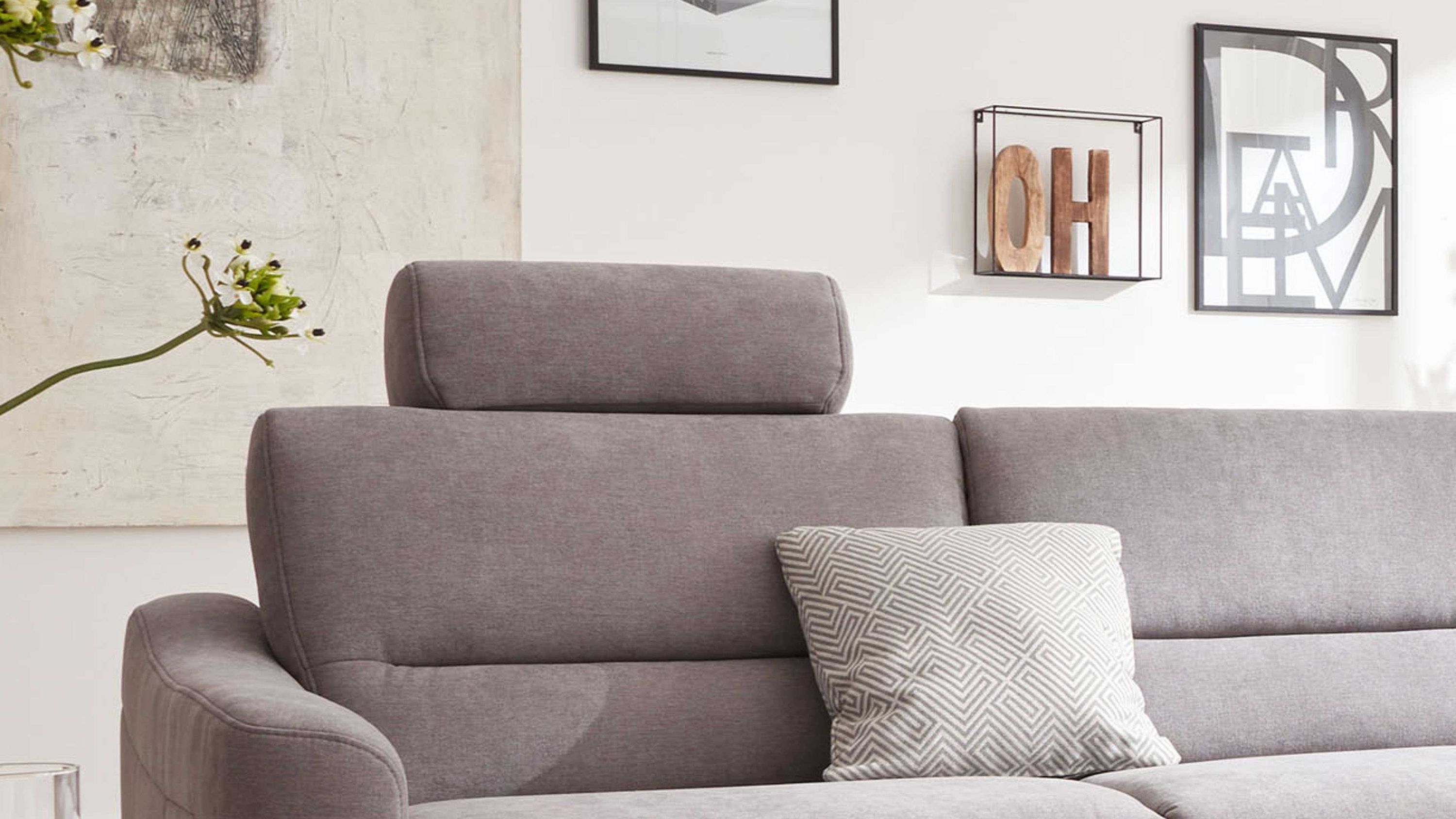 Graues Sofa mit verstellbarer Kopfstütze und einem gemusterten Kissen in einem hellen Raum