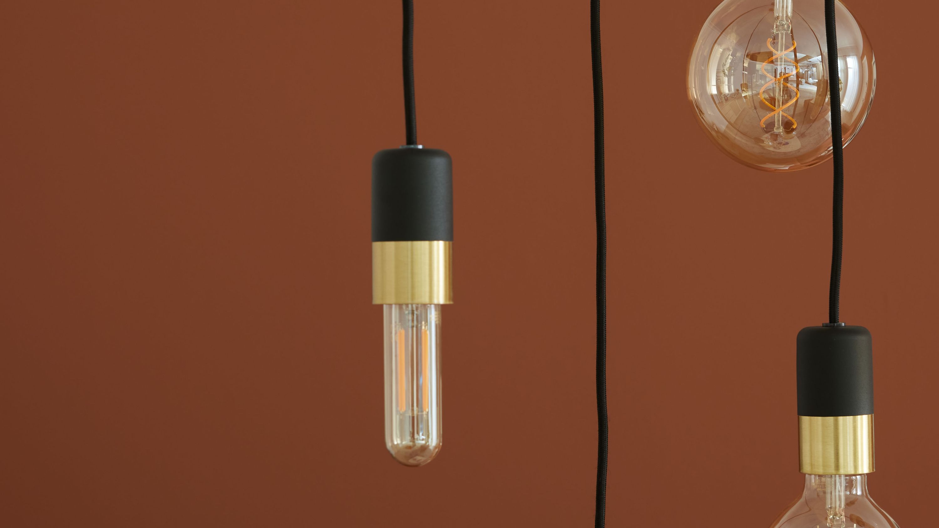 Hängeleuchten mit schwarzen und messingfarbenen Fassungen Drei hängende Lampen mit schwarzen und messingfarbenen Fassungen und sichtbaren Glühbirnen vor braunem Hintergrund