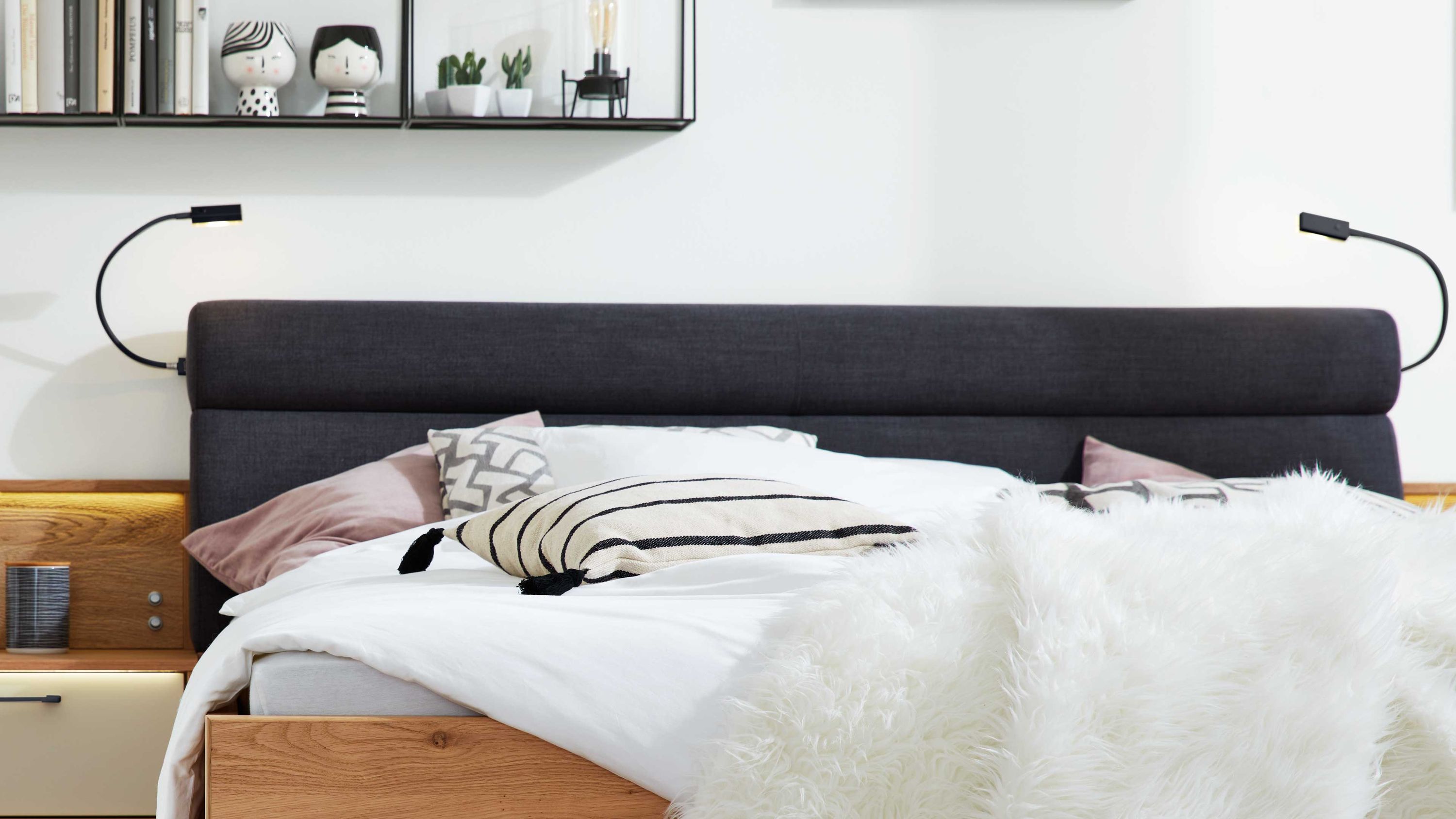 Zweiteiliges Flexleuchten-Set mit schwarzen flexiblen Armen an einem dunklen Polsterkopfteil über einem Bett