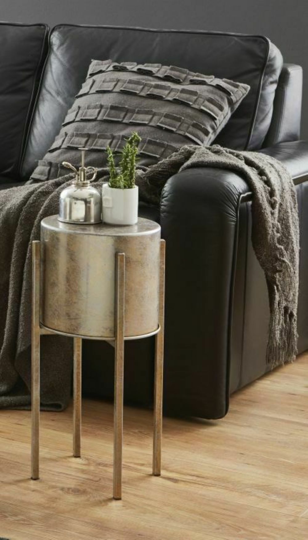 Blumensäule in Antikbronze neben dunklem Sofa platziert  dekoriert mit kleiner Pflanze und Kerze auf Holzfußboden