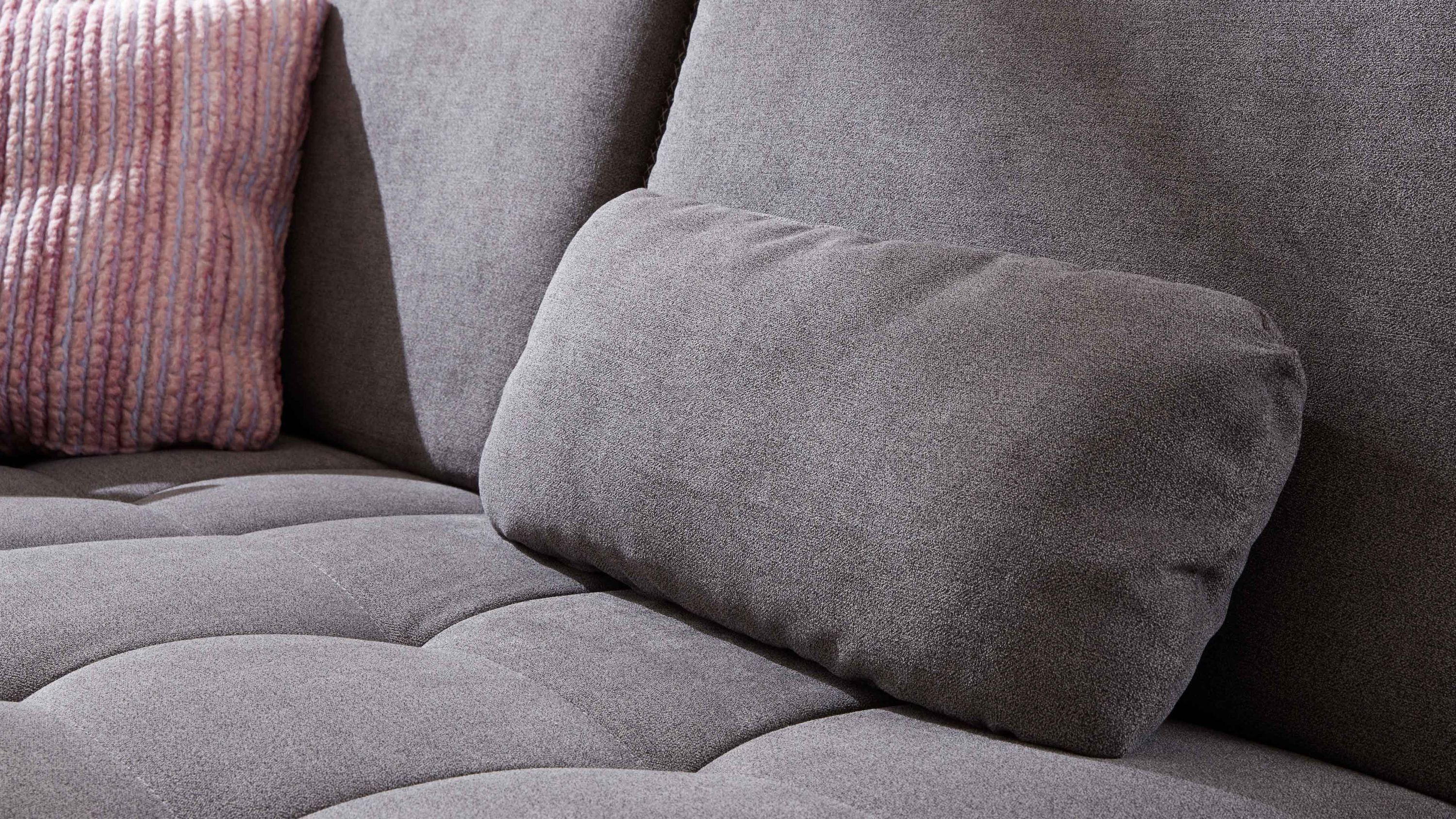 Rechteckiges Nierenkissen in schiefergrauer Farbe auf grauem Sofa mit gestepptem Sitz und rosafarbenem Kissen im Hintergrund