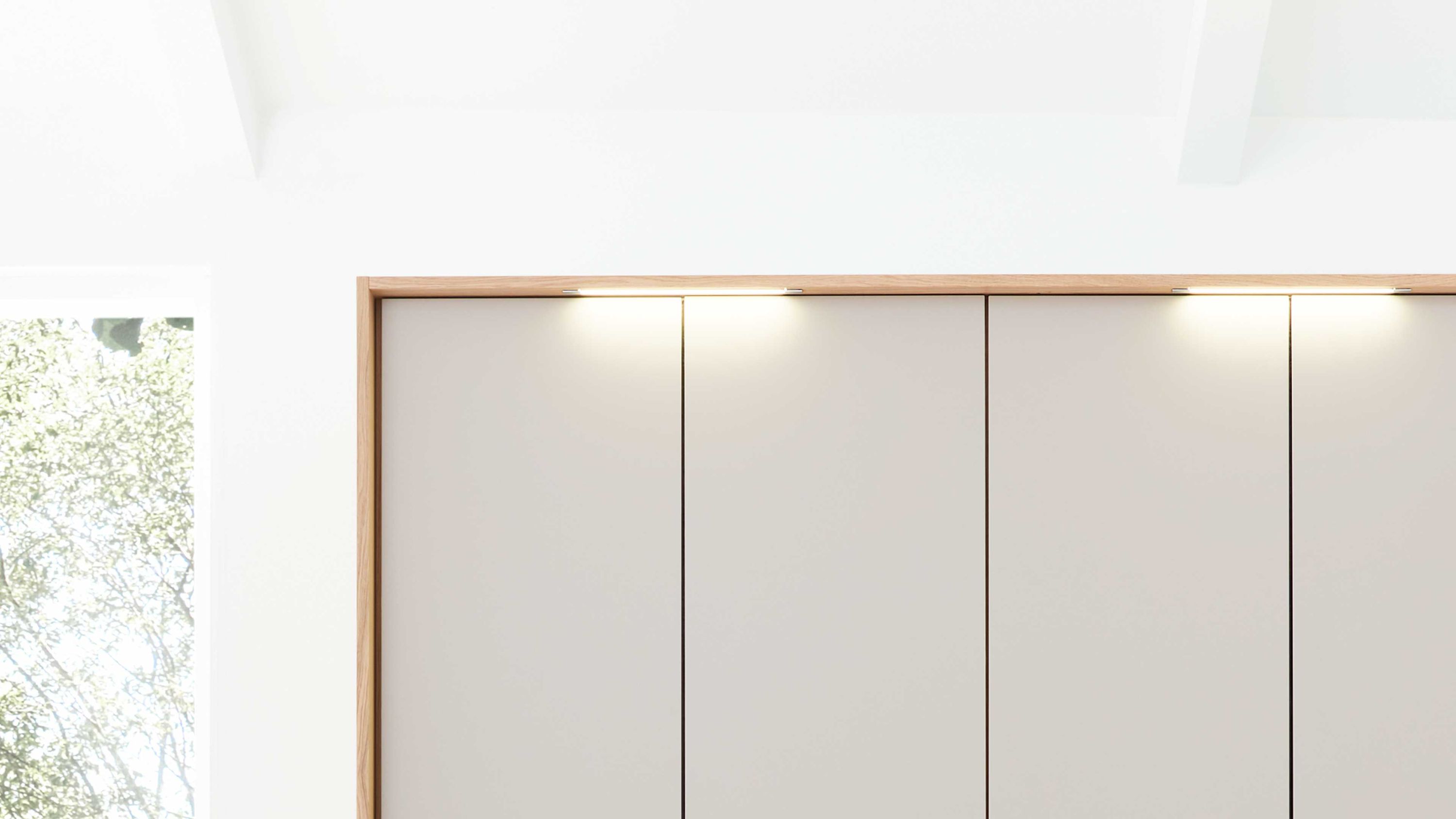 Schlafzimmerschrank mit vier hellen Türen und drei schmalen Stabbeleuchtungen oben