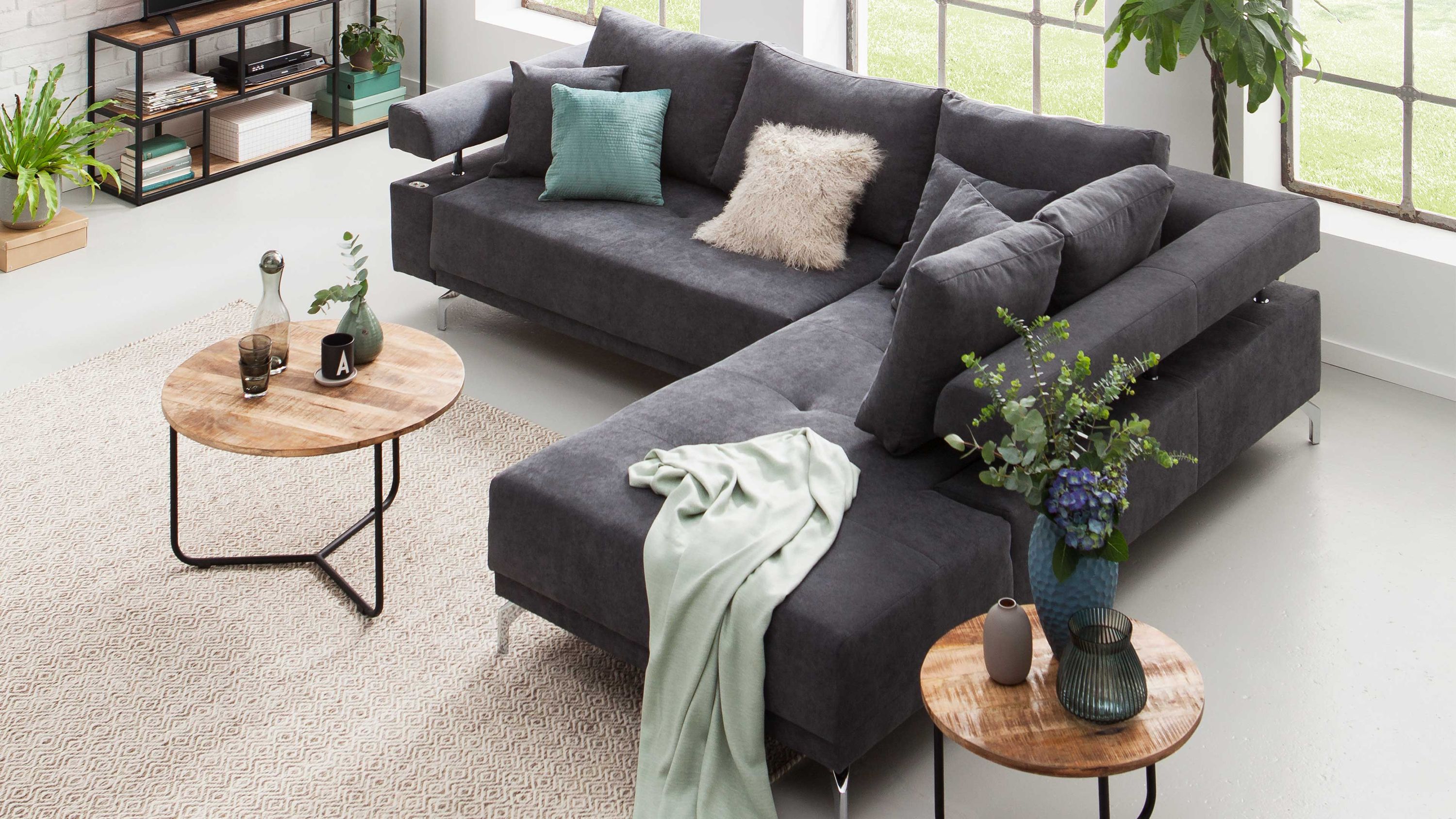 Anthrazitfarbenes Ecksofa mit Metallfüßen und mehreren Kissen in einem hellen Raum