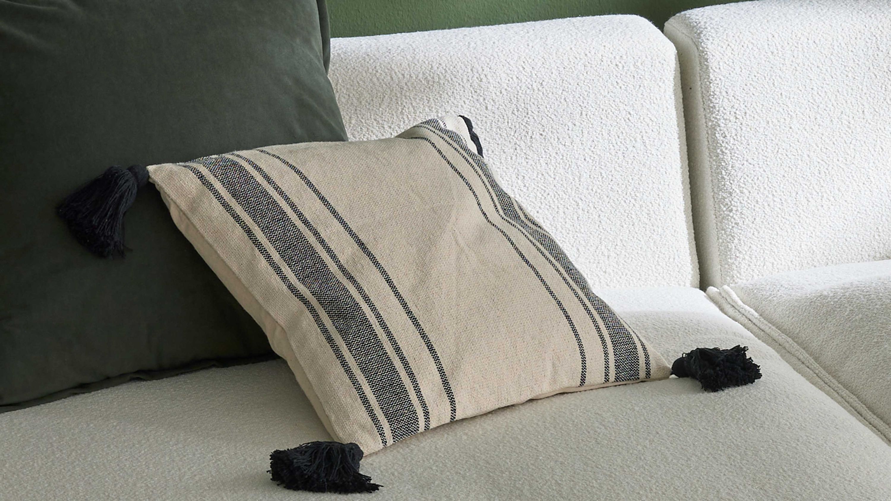 Quadratische Kissenhülle in Beige mit schwarzen Streifen und schwarzen Quasten an den Ecken