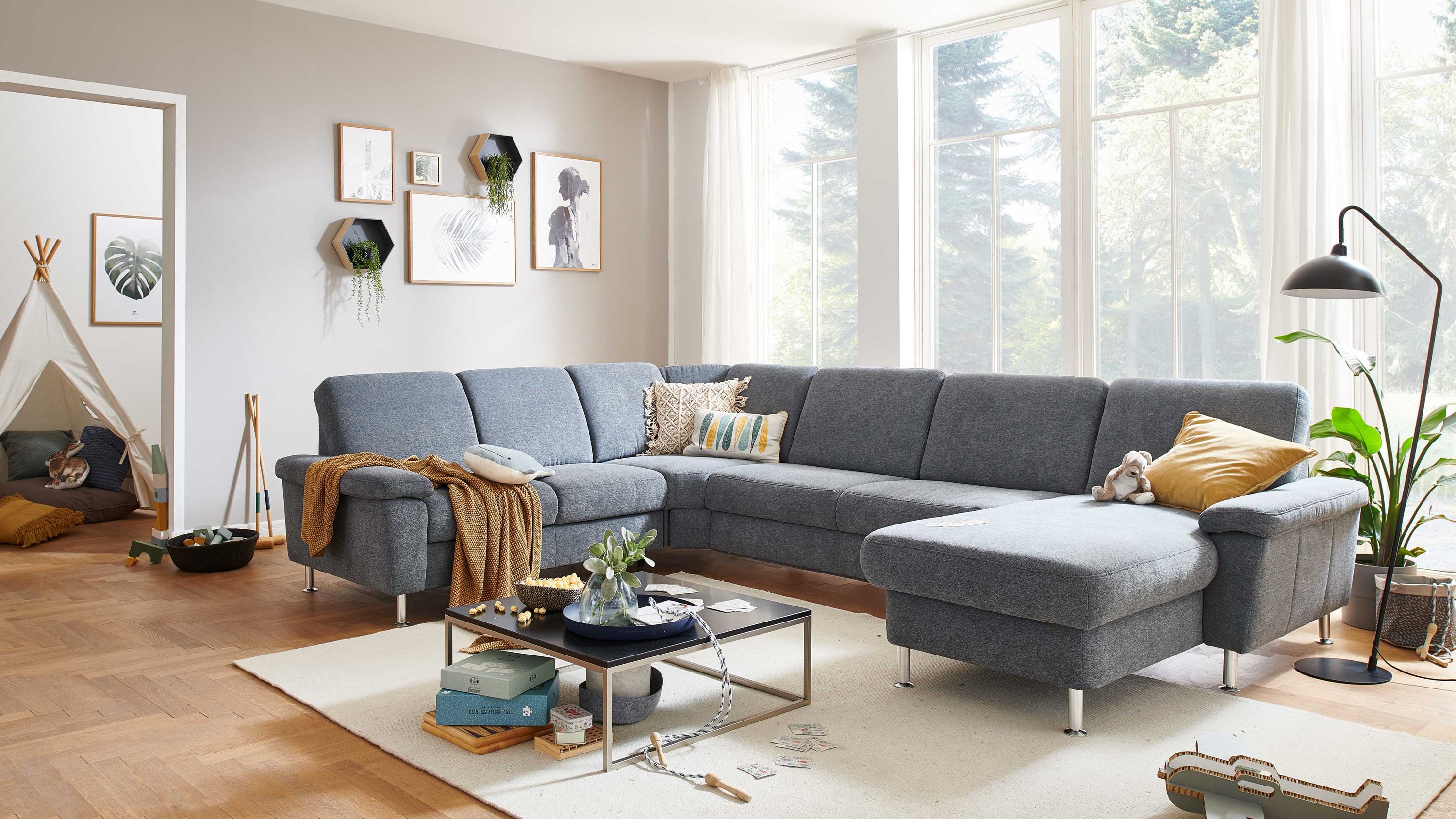 Großzügige Wohnlandschaft mit L-Form denimfarbener Polsterung und Metallfüßen in hellem Wohnzimmer