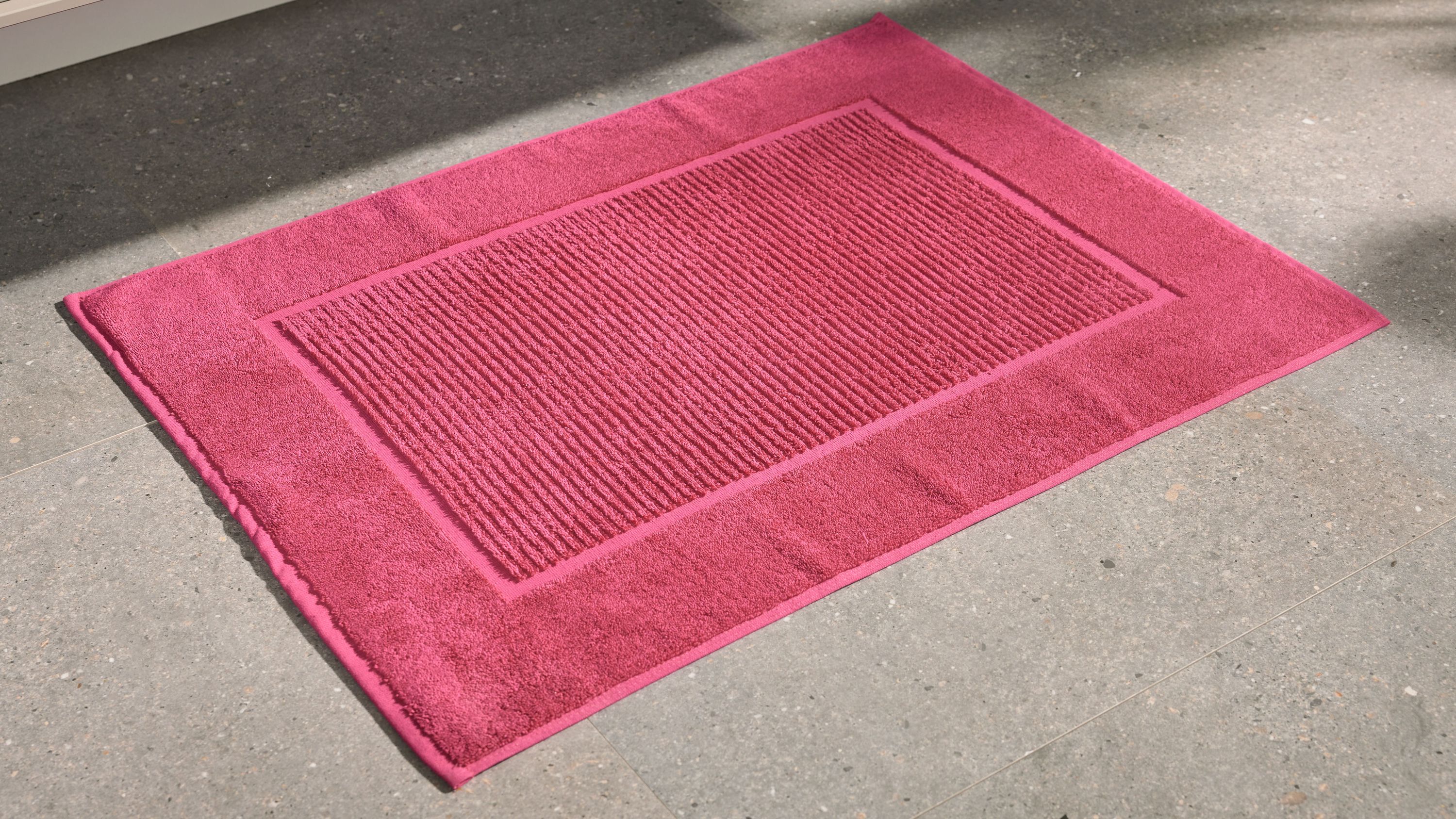 Rechteckiger Badvorleger in pink mit strukturiertem Mittelteil auf grauem Boden