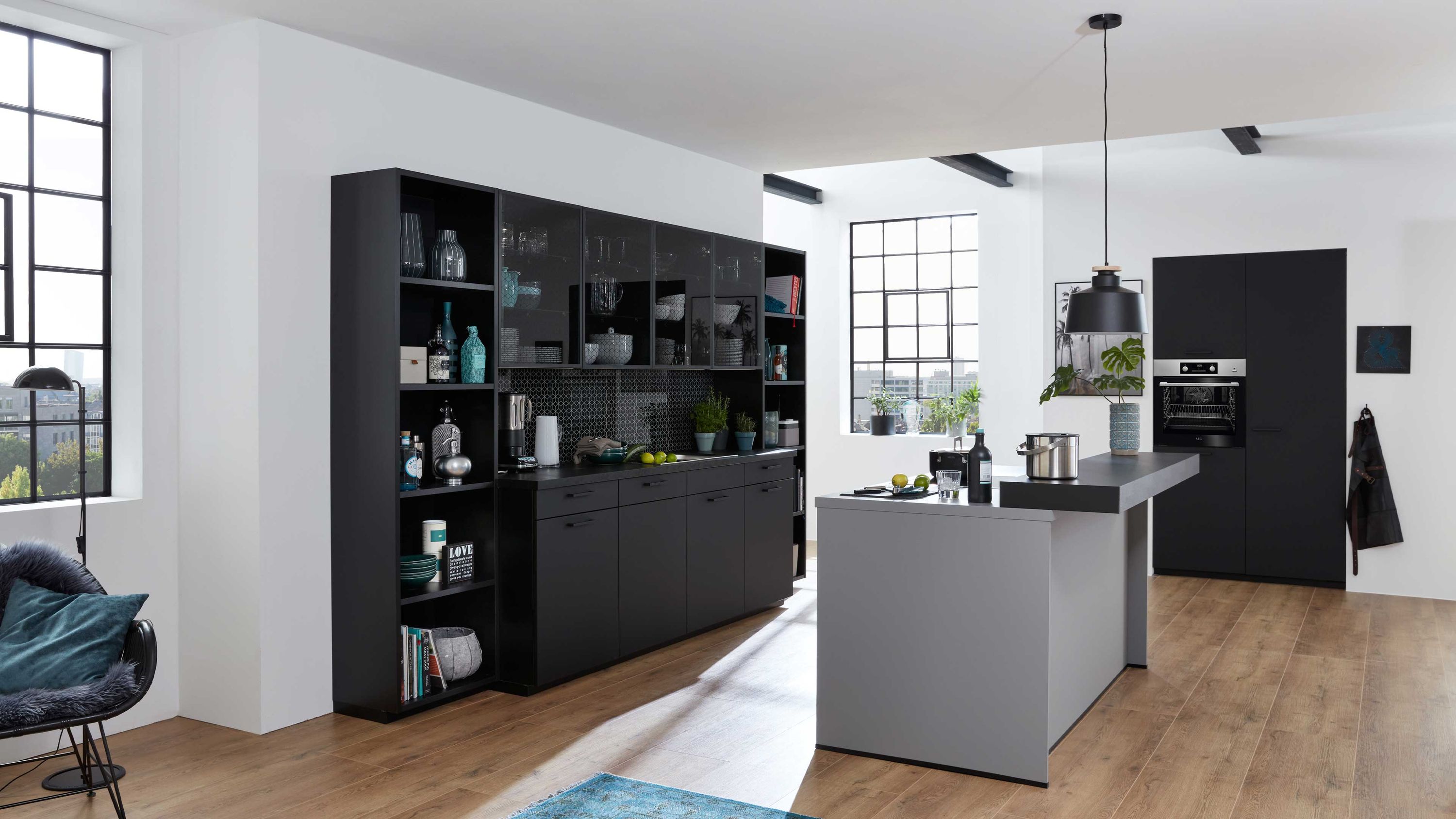 Moderne Küche mit schwarzen Fronten grauer Insel und hellem Holzboden Küche mit schwarzen Schränken grauer Insel hellem Holzboden Regalen Tageslicht durch große Fenster
