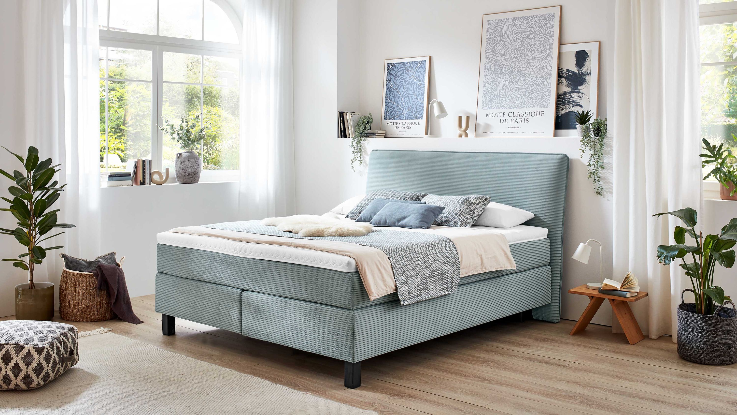 Boxspringbett mit gepolstertem Kopfteil und aquafarbenem Cordbezug in einem hellen Schlafzimmer