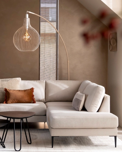 Ecksofa mit Bogenlampe in stilvollem Wohnzimmer. Helles Ecksofa mit Kissen steht vor brauner Wand, darüber moderne Bogenlampe und daneben runder Couchtisch.