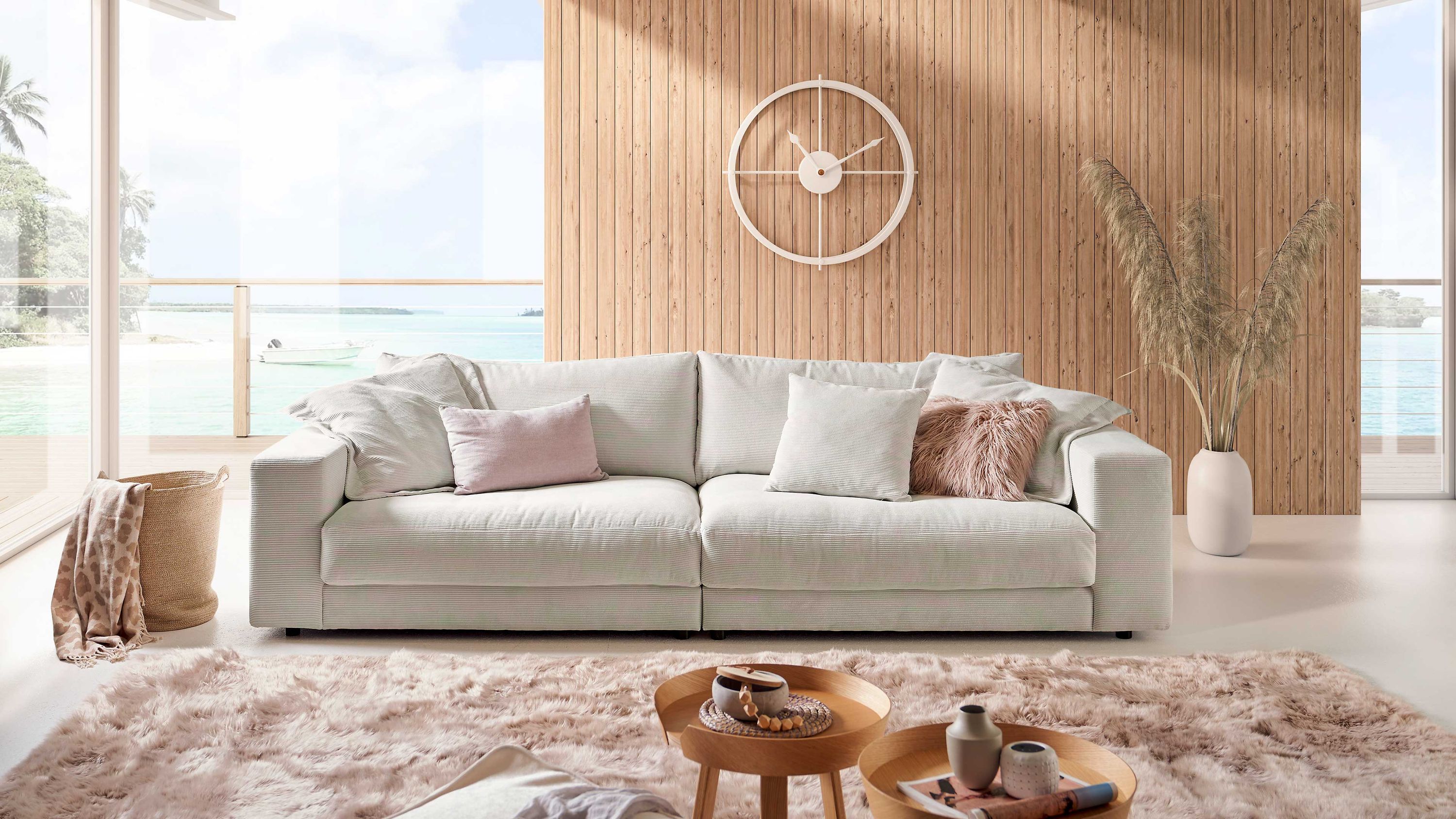Weißes großes Sofa mit Cordbezug Großes weißes Sofa mit Cordbezug und mehreren Kissen in einem hellen Raum mit Holzwand und Teppich