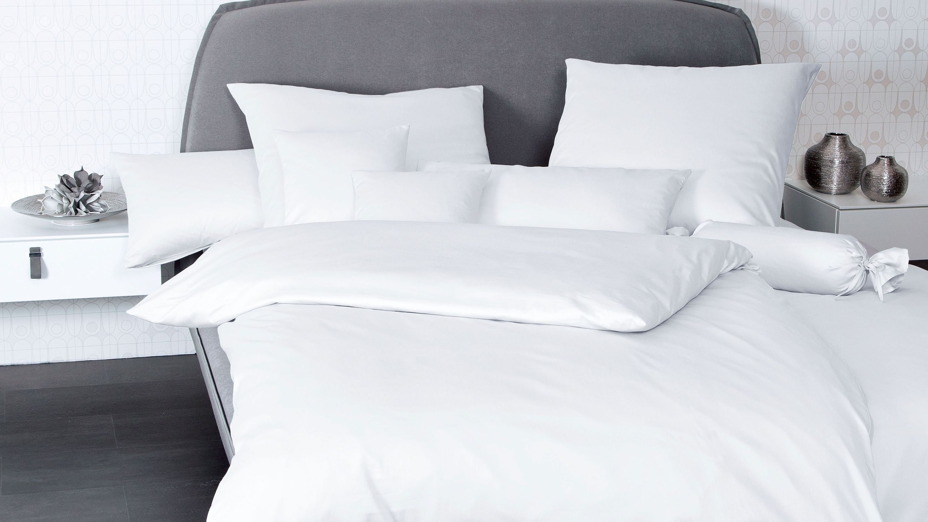 Weißes Bettwäsche-Set mit Kissen und Bettbezug auf grauem Polsterbett