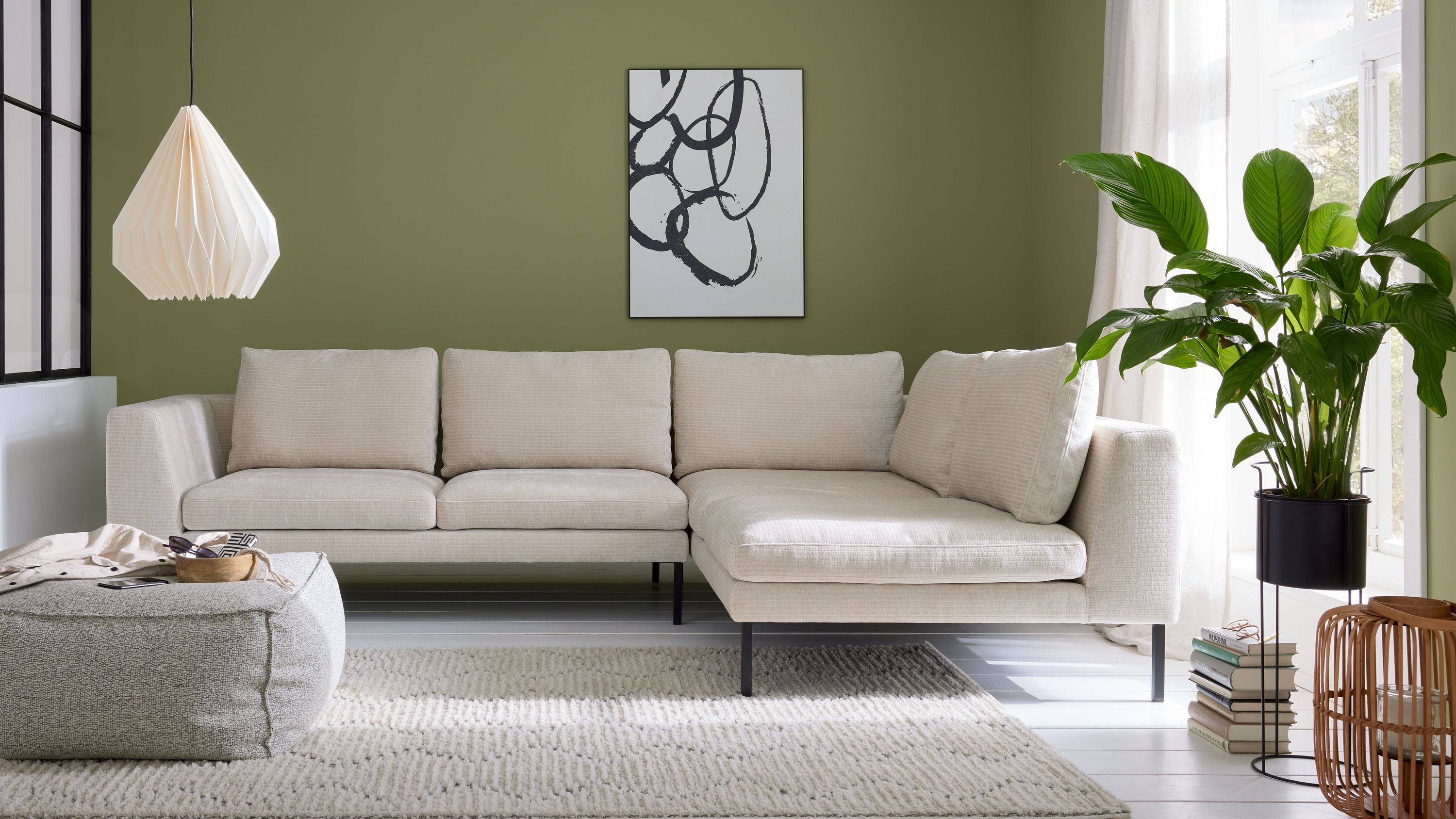 Ecksofa mit naturfarbenem Bezug und schwarzen Metallfüßen in hellem Wohnzimmer vor grüner Wand