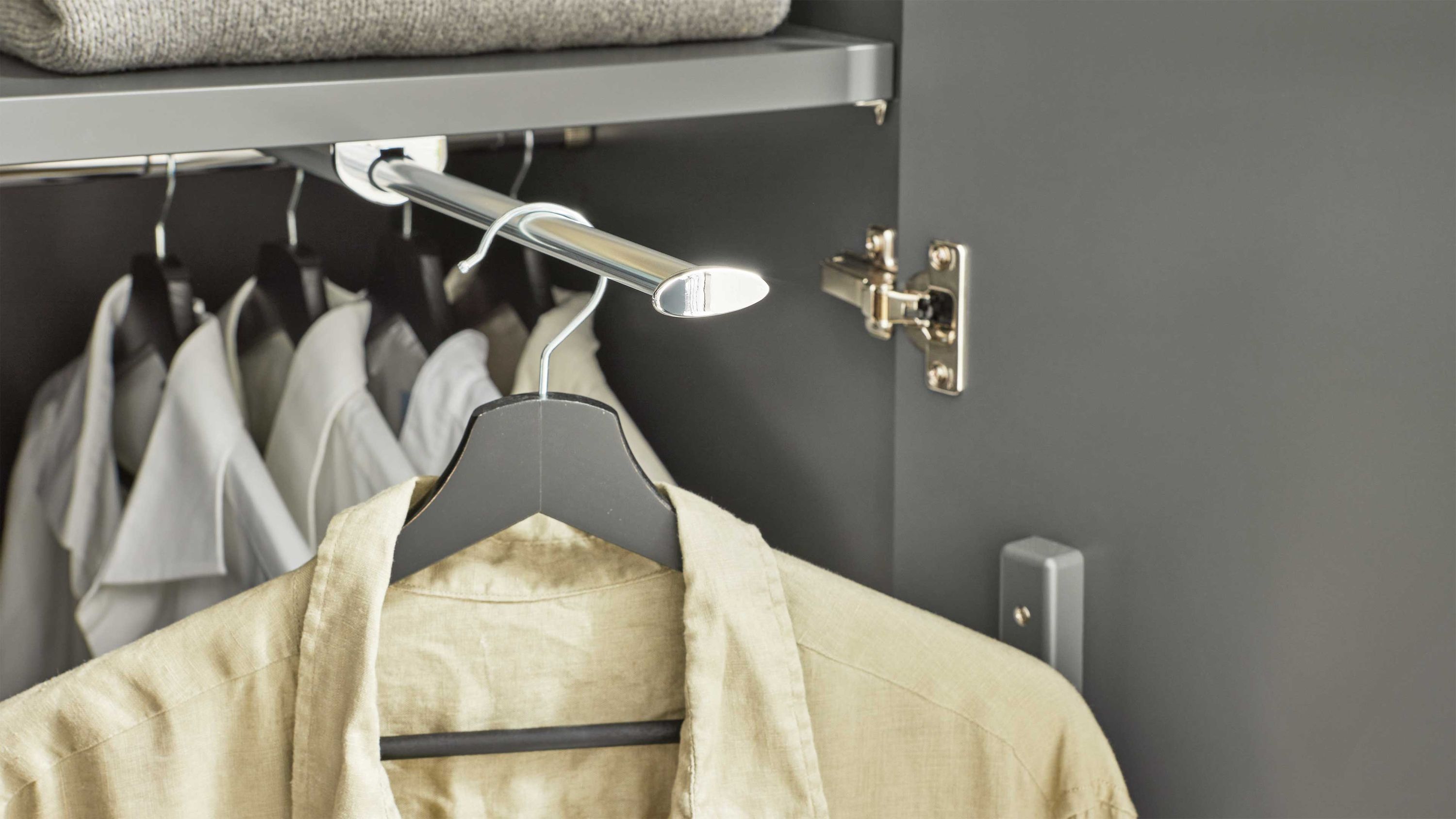 Ausziehbare Kleiderstange aus Metall in einem grauen Schrank mit aufgehängten Hemden