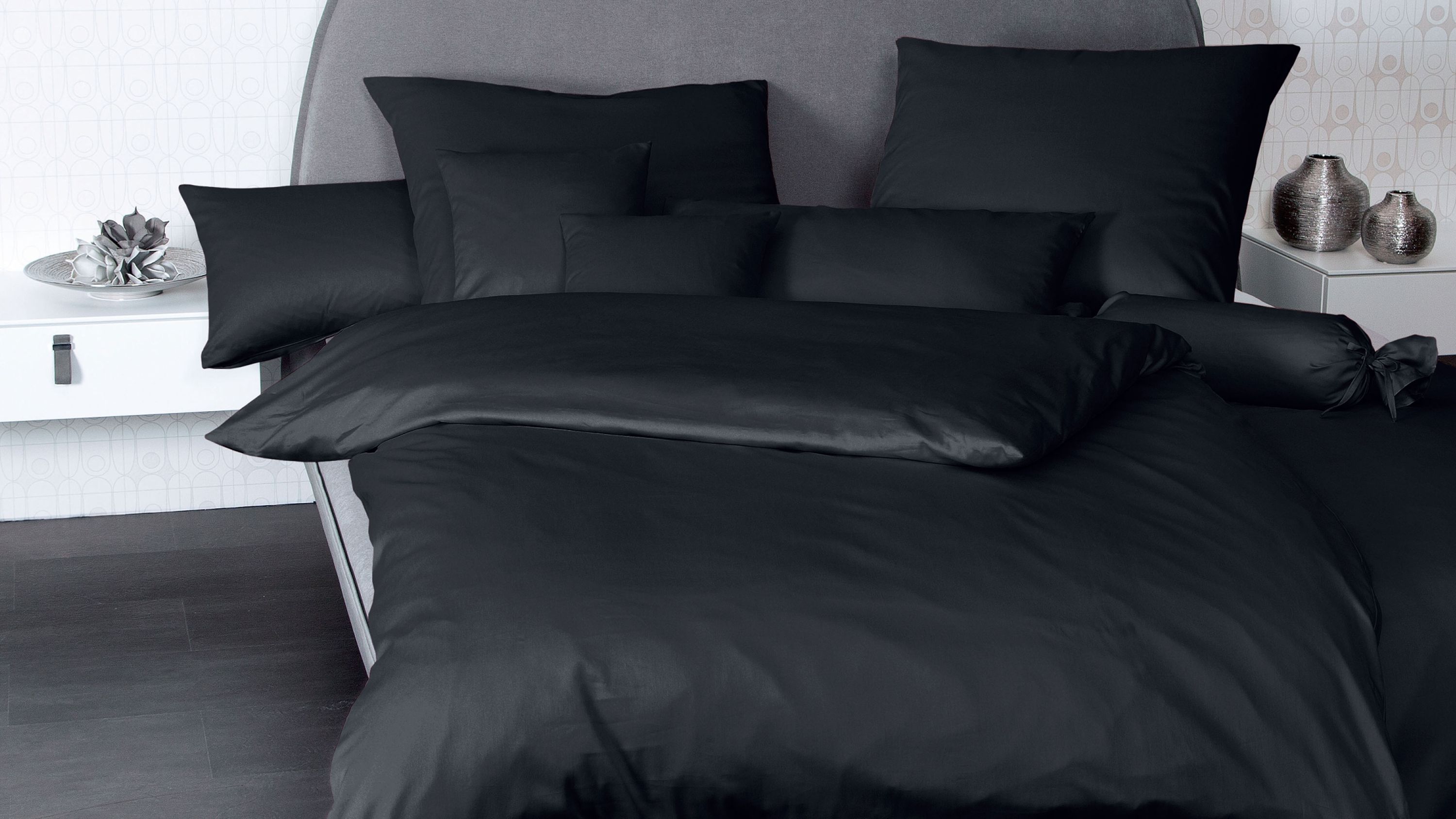 Schwarzes Bettwäsche-Set mit Kissen und Decke auf grauem Bett mit grauem Kopfteil