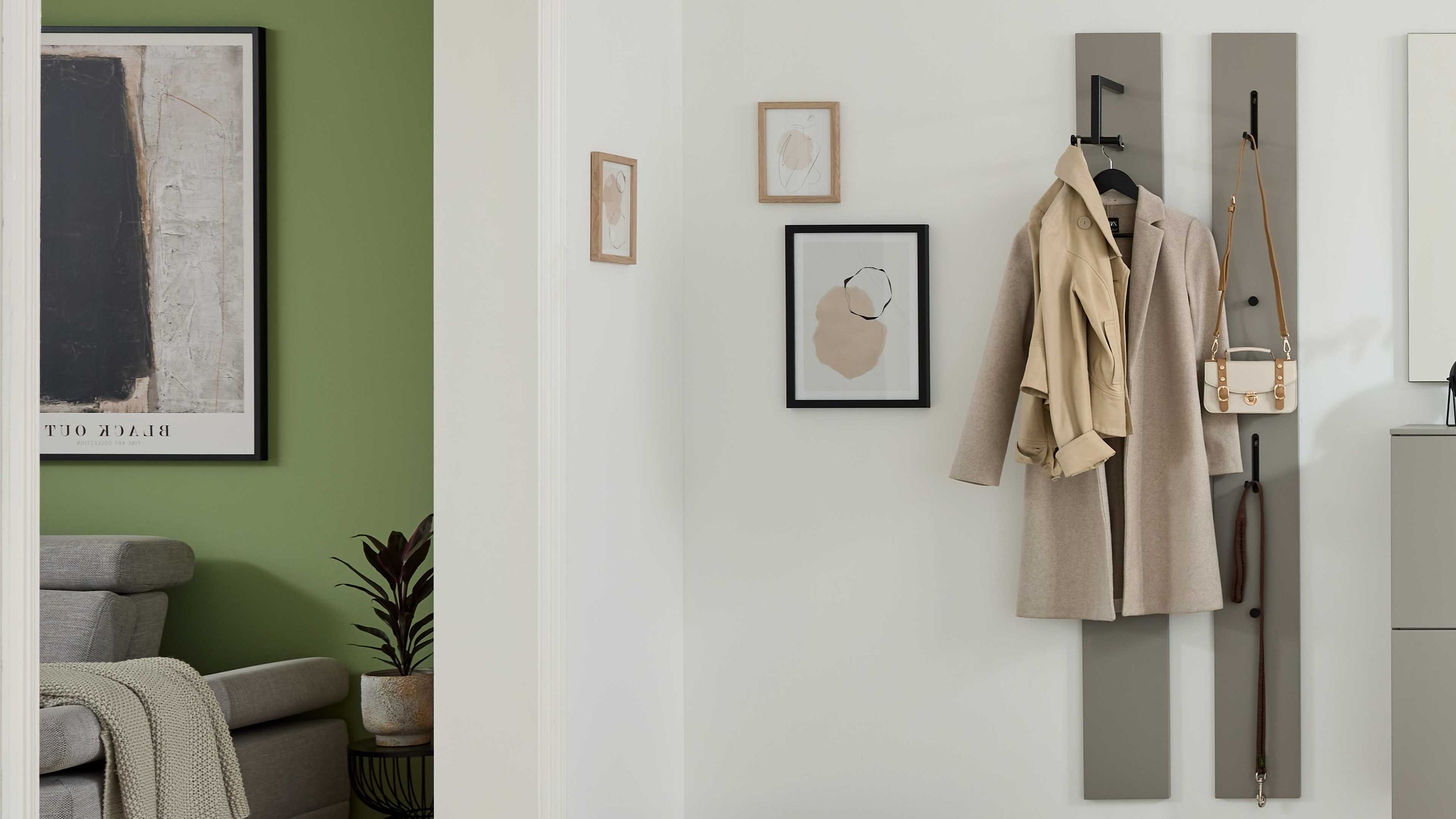 Wandgarderobe mit zwei graubeigen Paneelen und schwarzen Haken Zwei schmale graubeige Wandpaneele mit schwarzen Haken an denen Mäntel und eine Tasche hängen