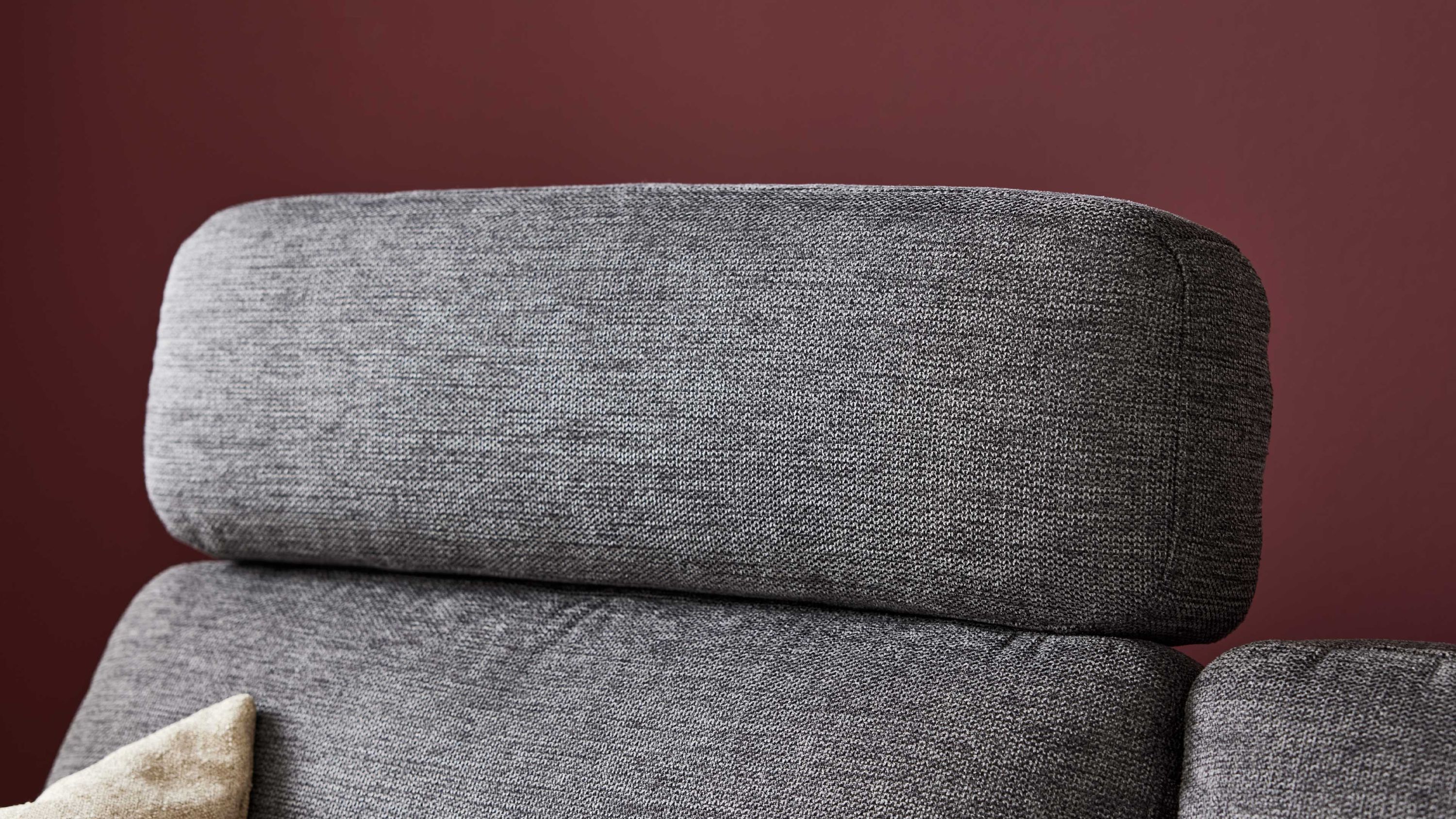Anthrazitfarbene Kopfstütze eines Schlafsofas mit Stoffbezug vor roter Wand