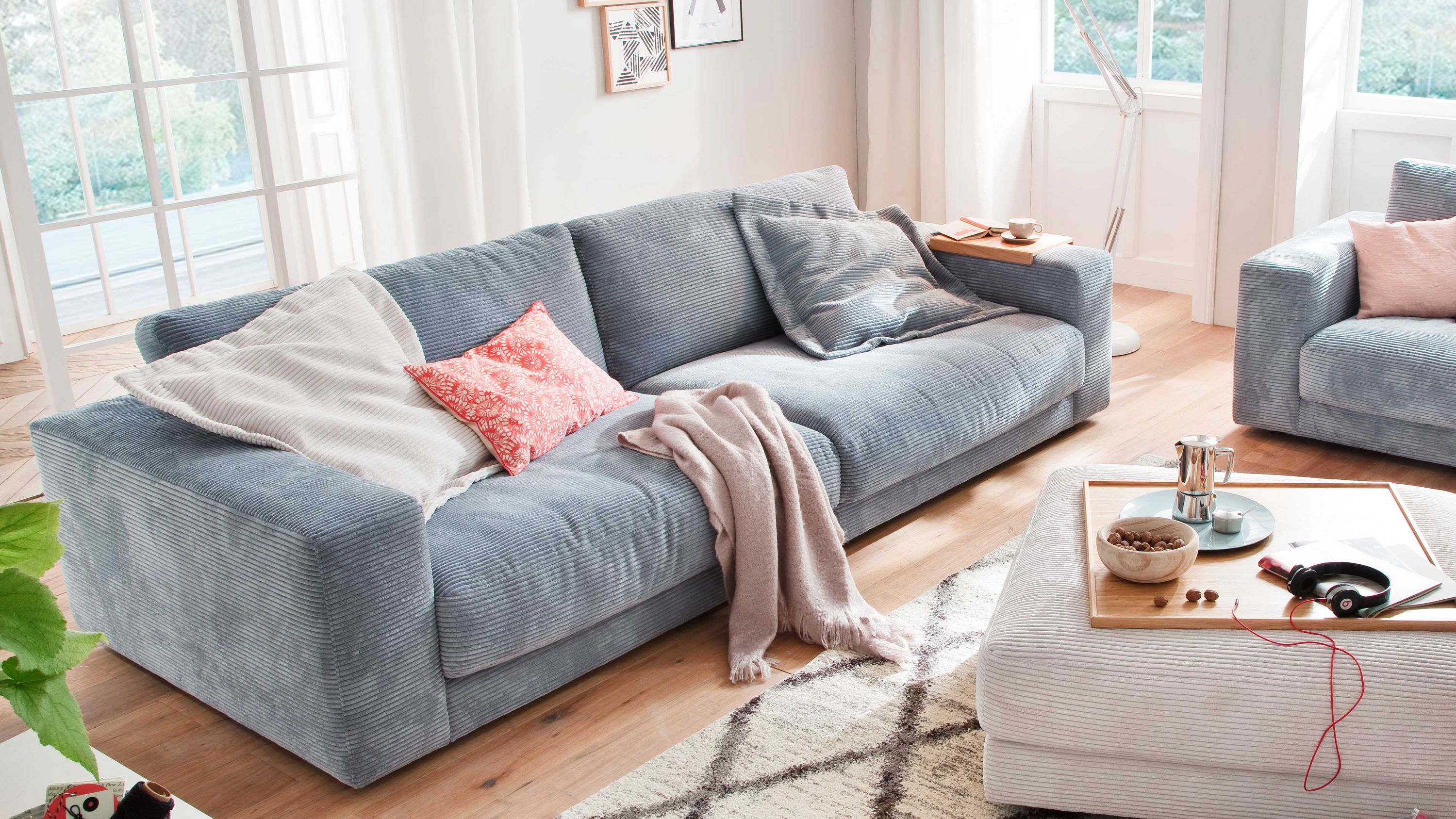 Hellblaues großes Sofa mit Cordbezug Großes hellblaues Sofa mit Cordbezug und mehreren Kissen in einem hellen Wohnzimmer