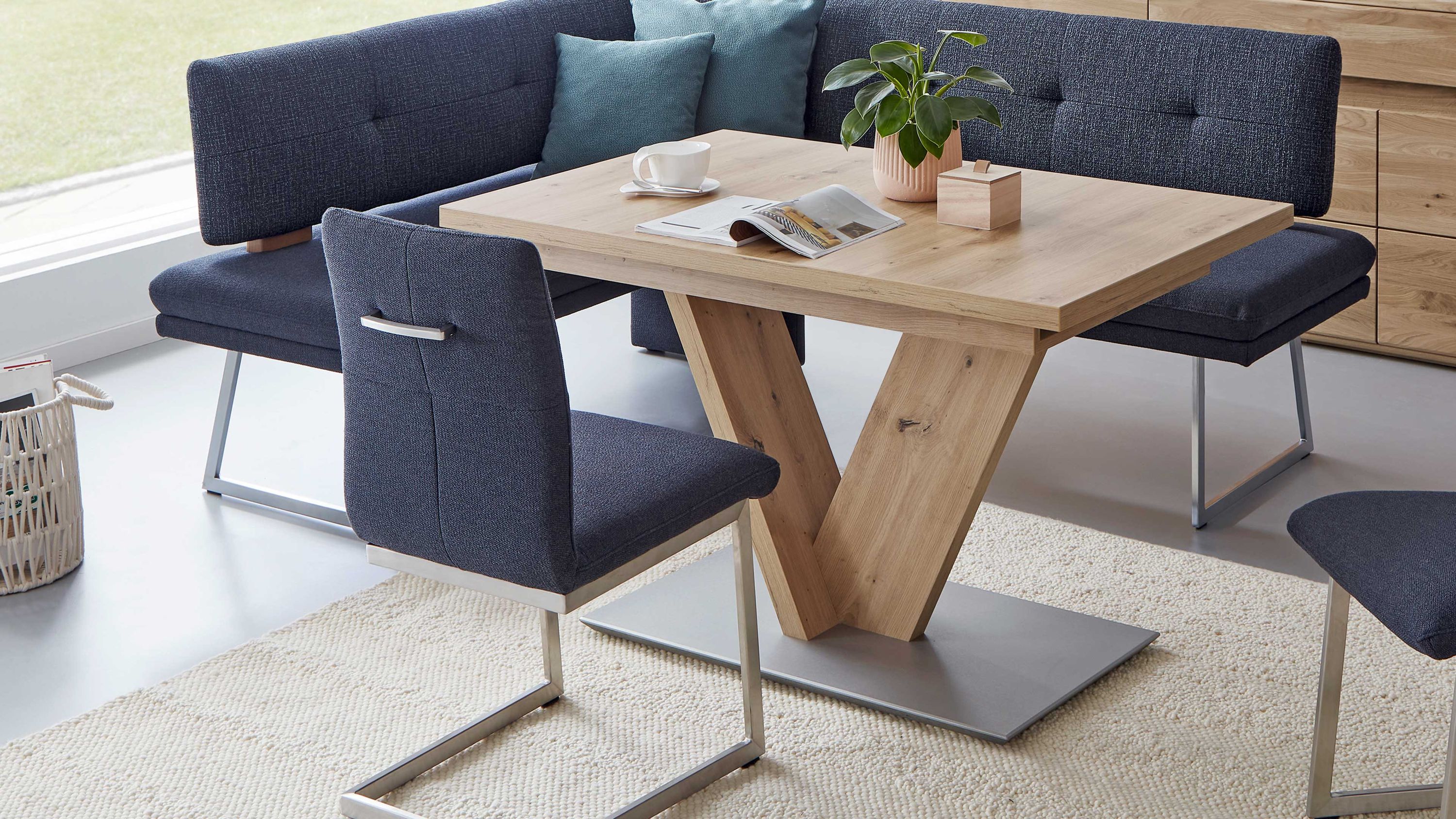 Esstisch mit V-förmigem Holzgestell und grauer Polsterbank Rechteckiger Esstisch mit V-förmigem Holzgestell und grauer Polsterbank und Stühlen mit Metallbeinen
