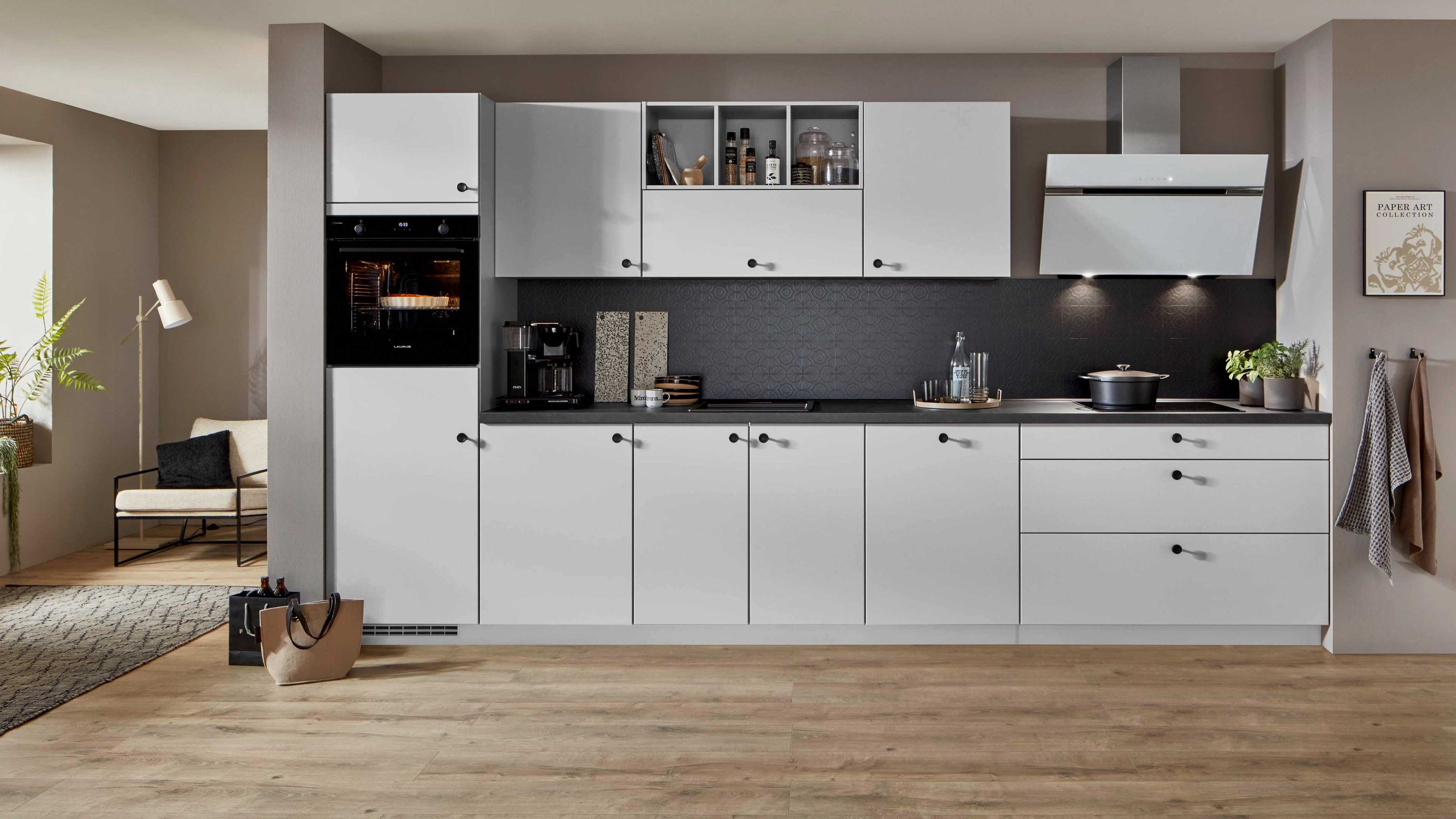 Küche mit weißen Fronten dunkler Arbeitsplatte und Edelstahlgeräten Weiße Schränke schwarze Platte Einbauofen Kaffeemaschine Dunstabzug Holzfußboden Pflanzen Wandbilder