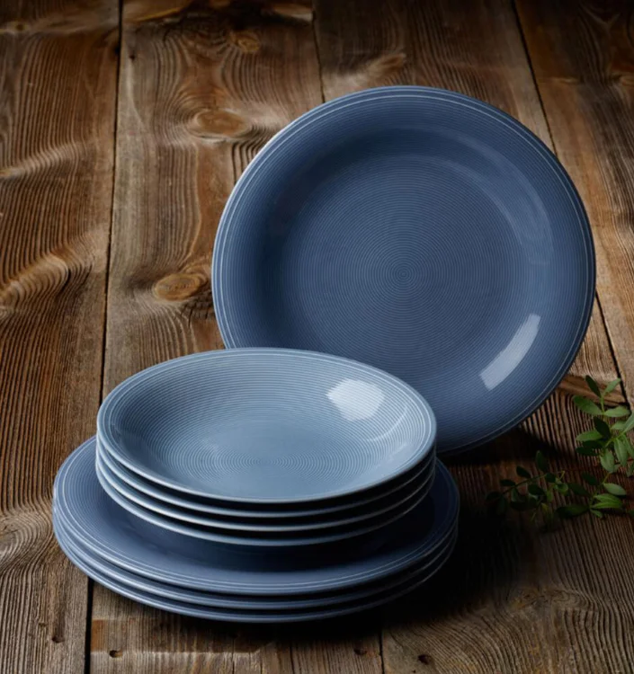 Blaues Keramikteller-Set mit feiner Struktur auf rustikalem Holztisch, bestehend aus flachen und tiefen Tellern.
