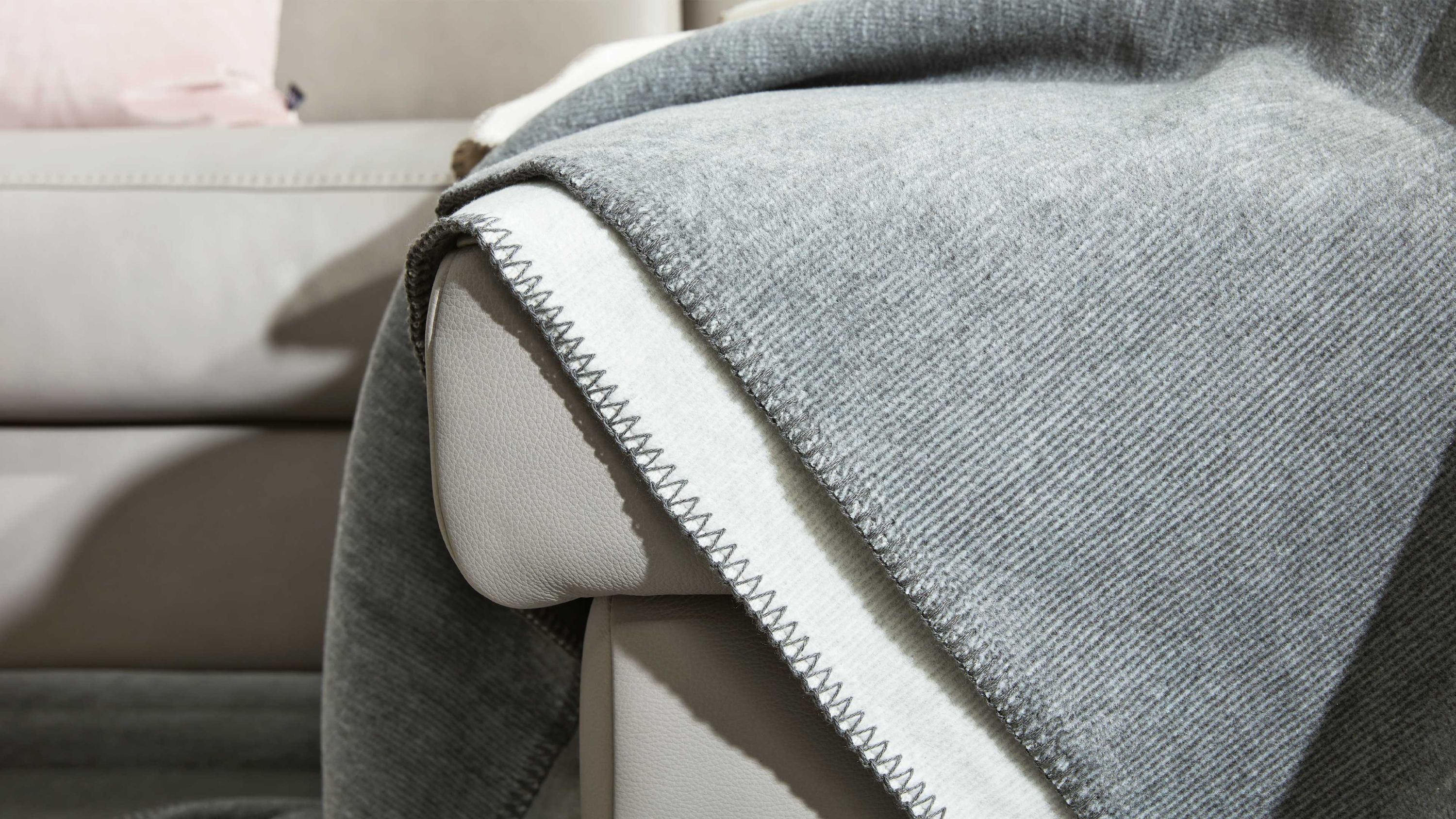 Hellgraue und beige Wohndecke mit Zickzacknaht auf hellgrauem Sofa