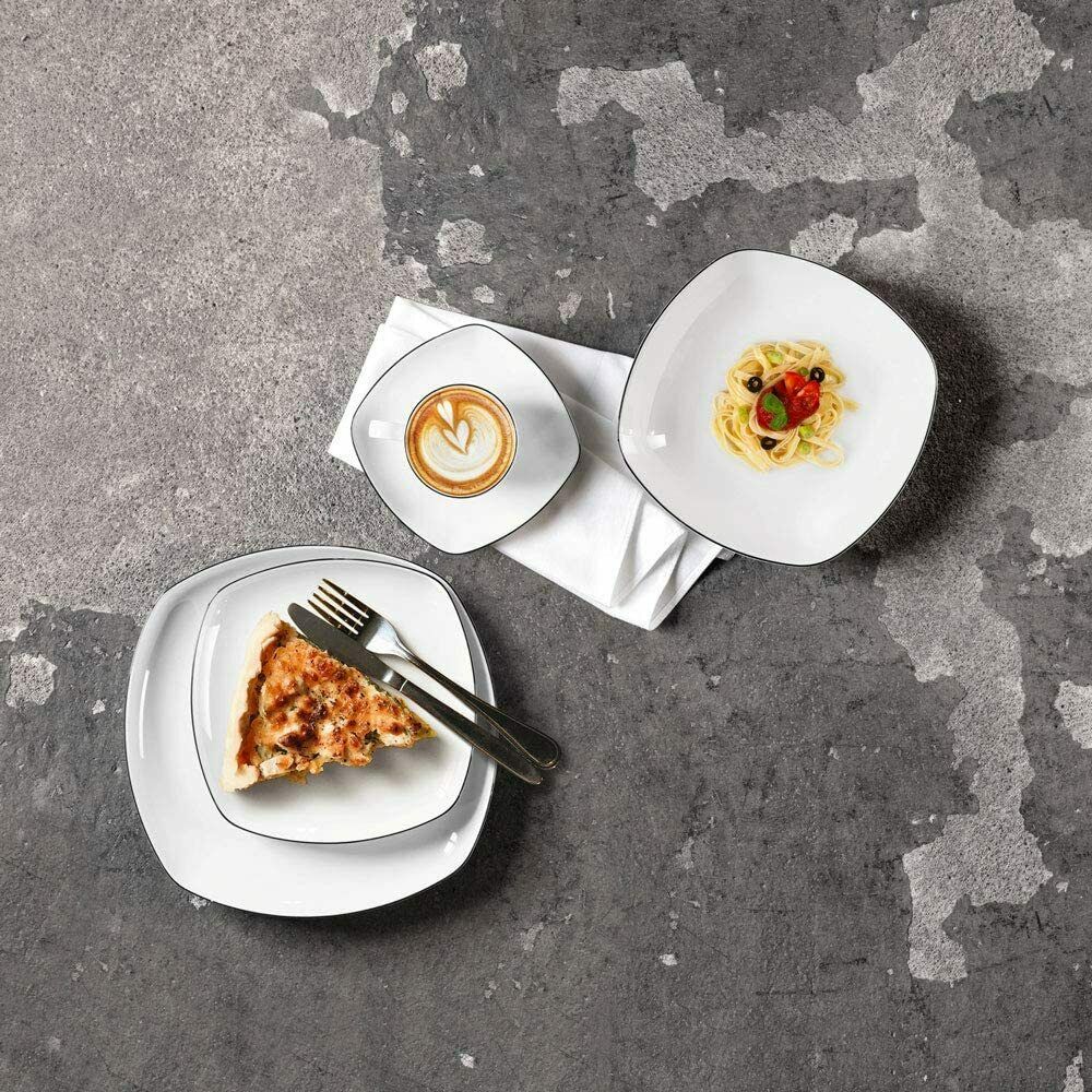 Weißes Geschirr mit Cappuccino, kleiner Portion Pasta und Kuchenstück auf grauem Betonuntergrund, Besteck liegt daneben