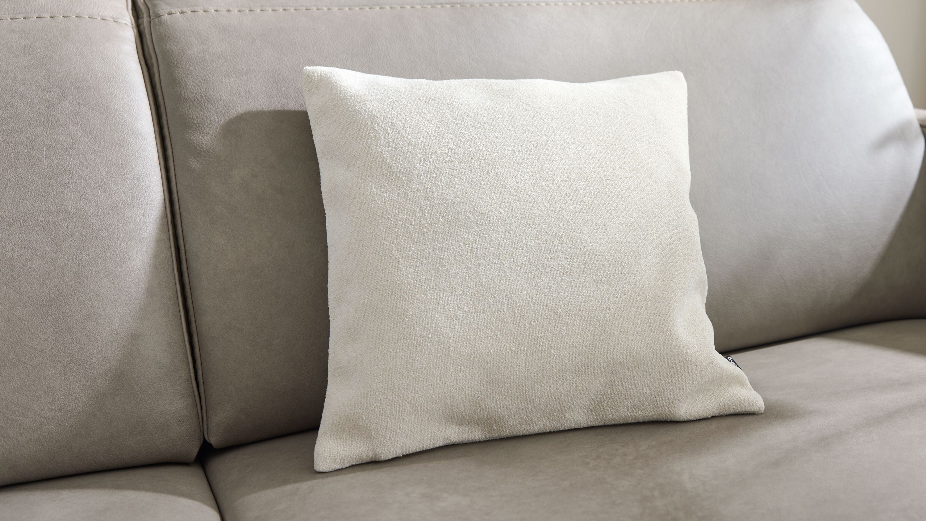 Weißes quadratisches Kissen auf Sofa Quadratisches weißes Kissen mit strukturierter Oberfläche auf grauem Sofa