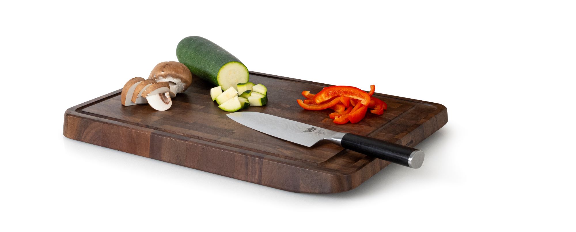 Rechteckiges Tranchierbrett mit Messer Champignons Zucchini und Paprika schräg von oben rechts aufgenommen