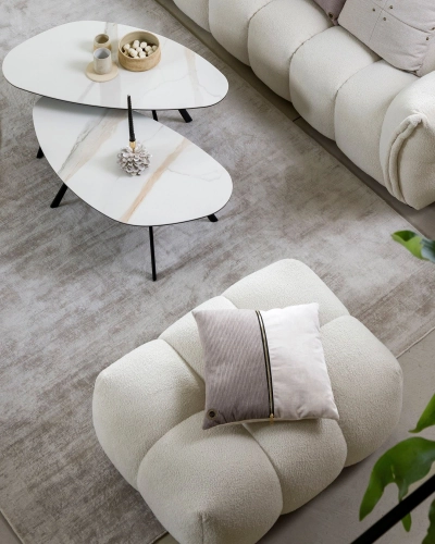 Polsterhocker und Couchtische im modernen Wohnzimmer. Modernes Wohnzimmer mit cremefarbenem Polsterhocker, Zierkissen und zwei weißen Couchtischen auf einem hellen Teppich.