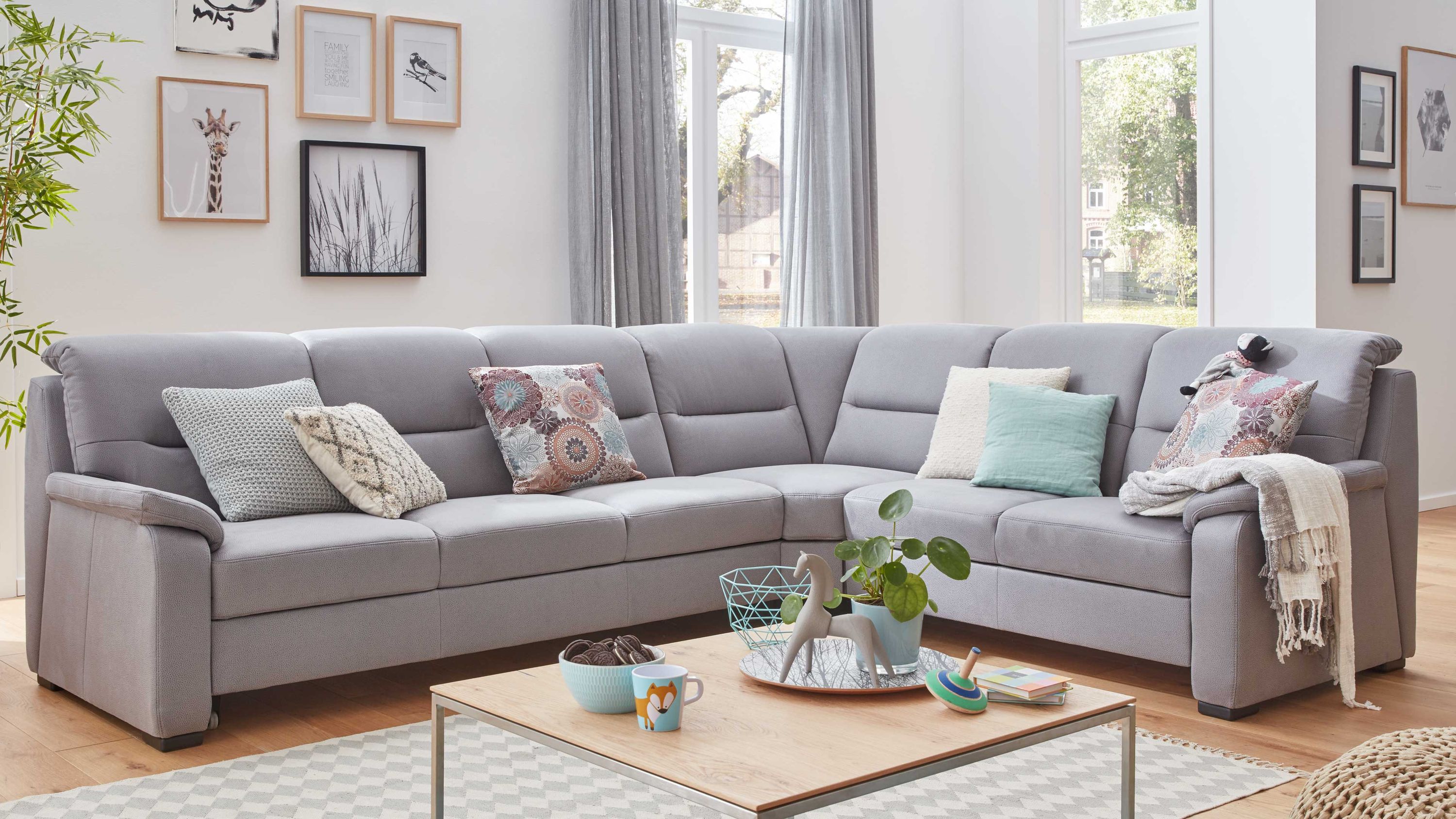 Ecksofa mit grauer Mikrofaserpolsterung schwarzer Holzfüße und mehreren Kissen in einem hellen Wohnzimmer