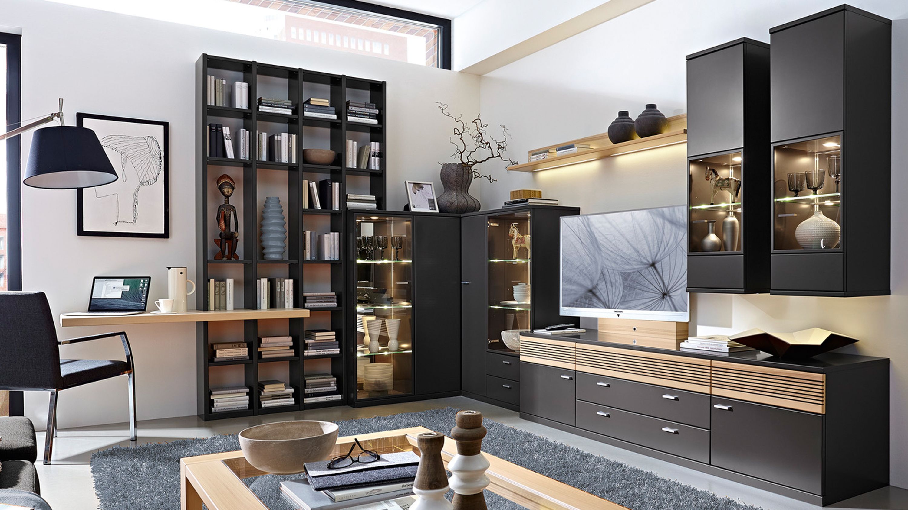 Eck-Wohnkombination mit Regalen und Vitrinen in Graphit und Holz Eck-Wohnkombination mit graphitfarbenen Fronten und hellen Holzakzenten bestehend aus Regalen Vitrinen und Sideboard