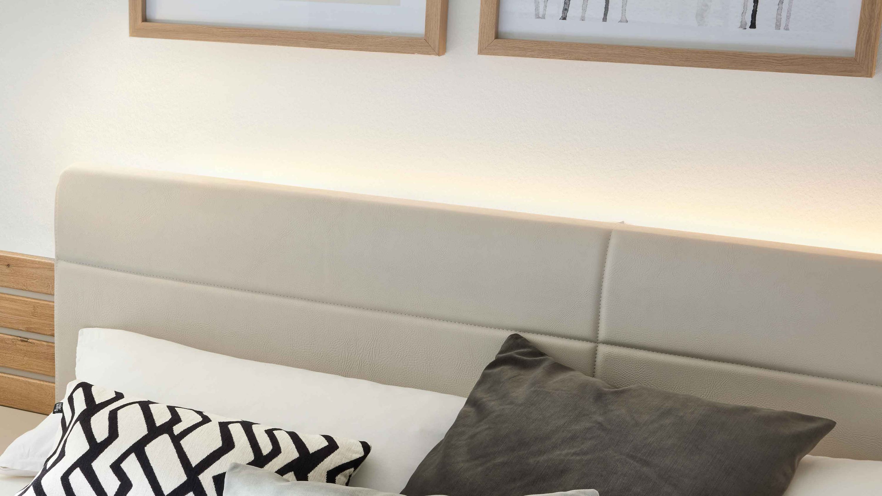 Beige gepolstertes Kopfteil mit integrierter Beleuchtung über einem Bett mit weißen und grauen Kissen
