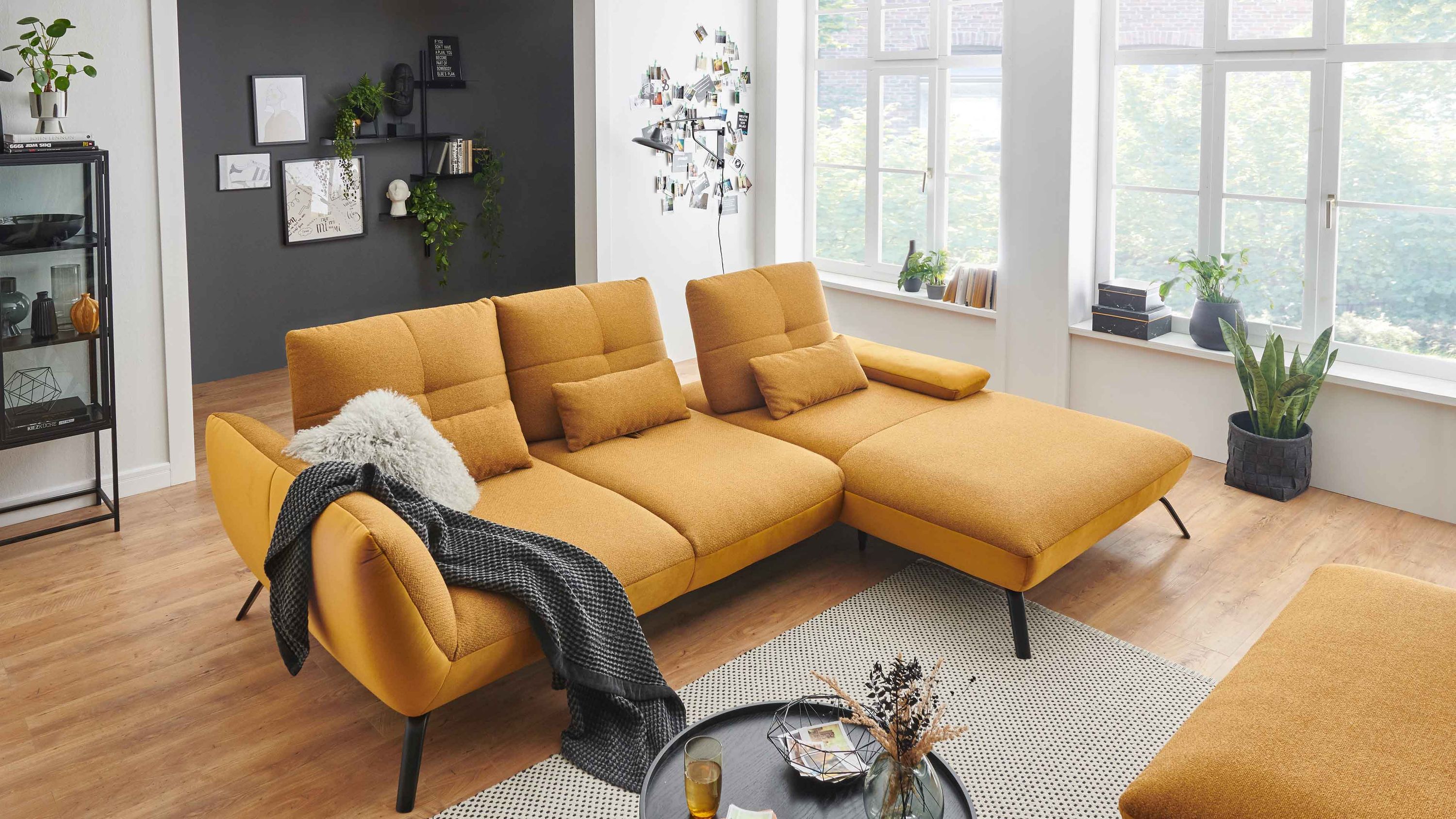 Ecksofa mit senffarbenem Bezug und schwarzen Metallbeinen in modernem Wohnzimmer mit großen Fenstern