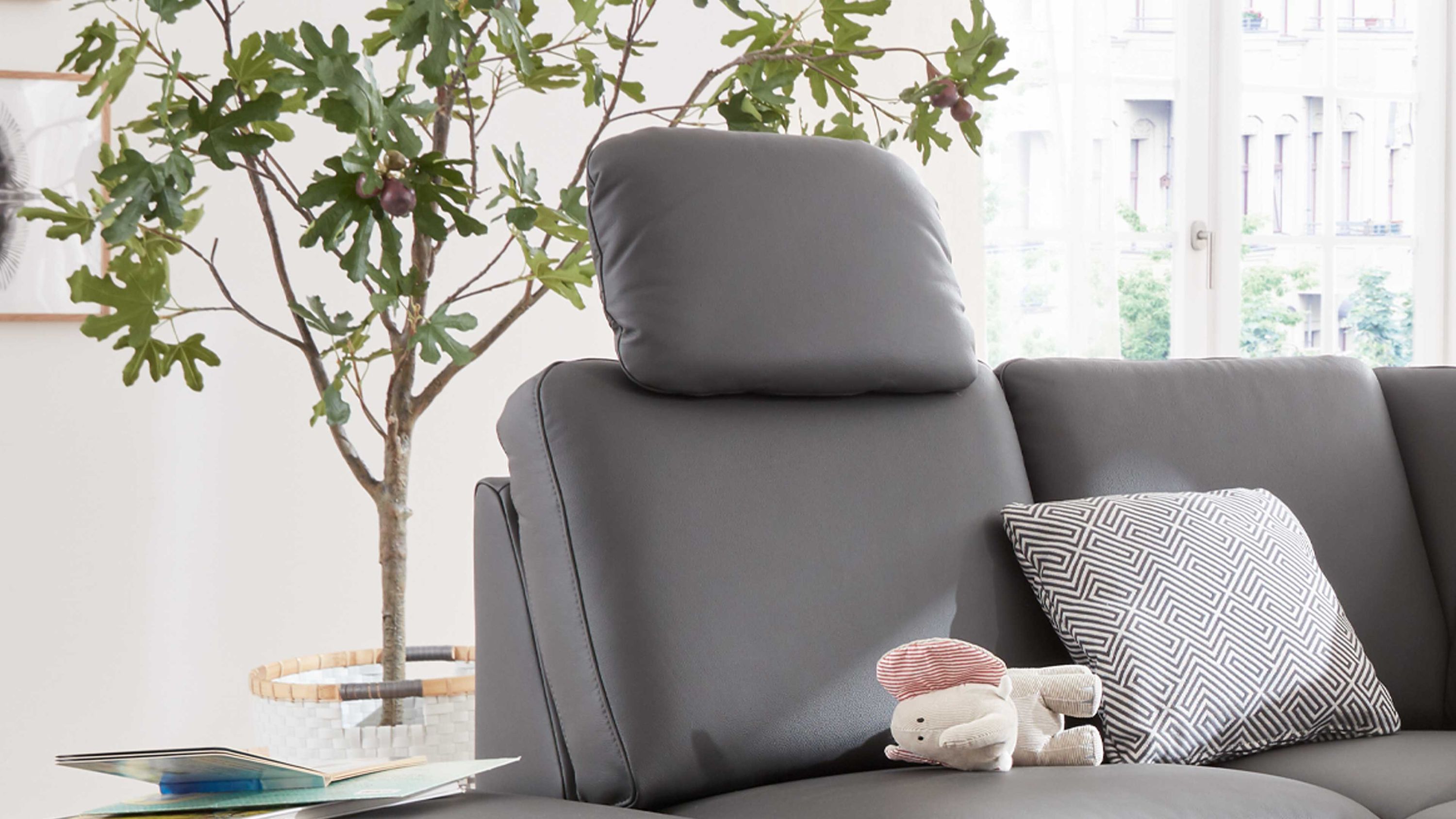 Anthrazitfarbene Kopfstütze auf einem Sofa mit Kissen und Stofftier