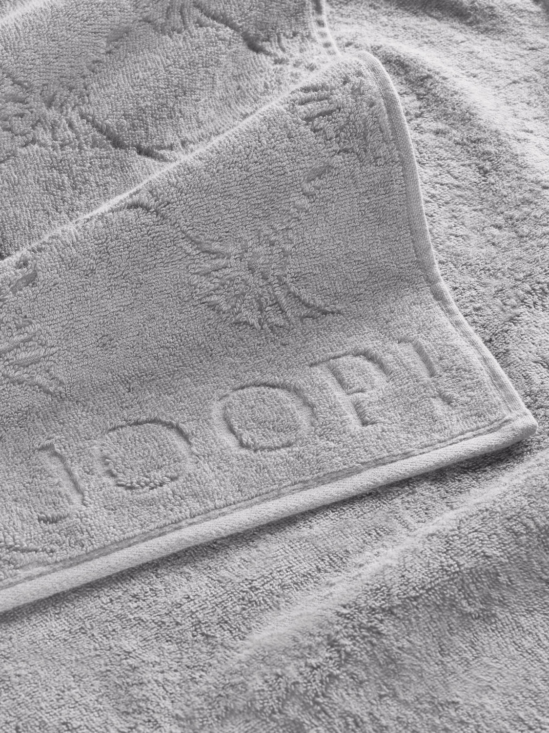 Graues Handtuch mit geprägtem „JOOP!“-Schriftzug Nahaufnahme eines grauen Handtuchs mit geprägtem „JOOP!“-Logo und strukturiertem Muster.