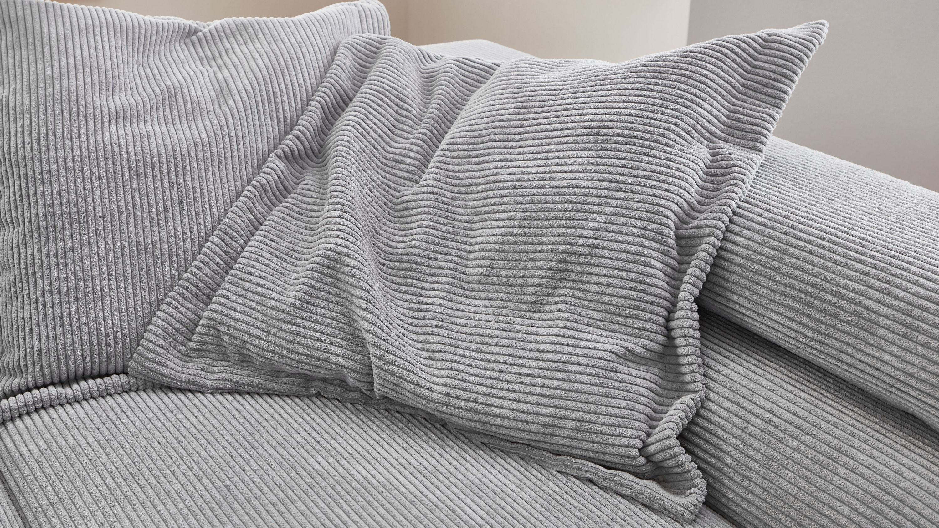 Quadratisches Kissen mit grauem Cordbezug auf grauem Cordsofa