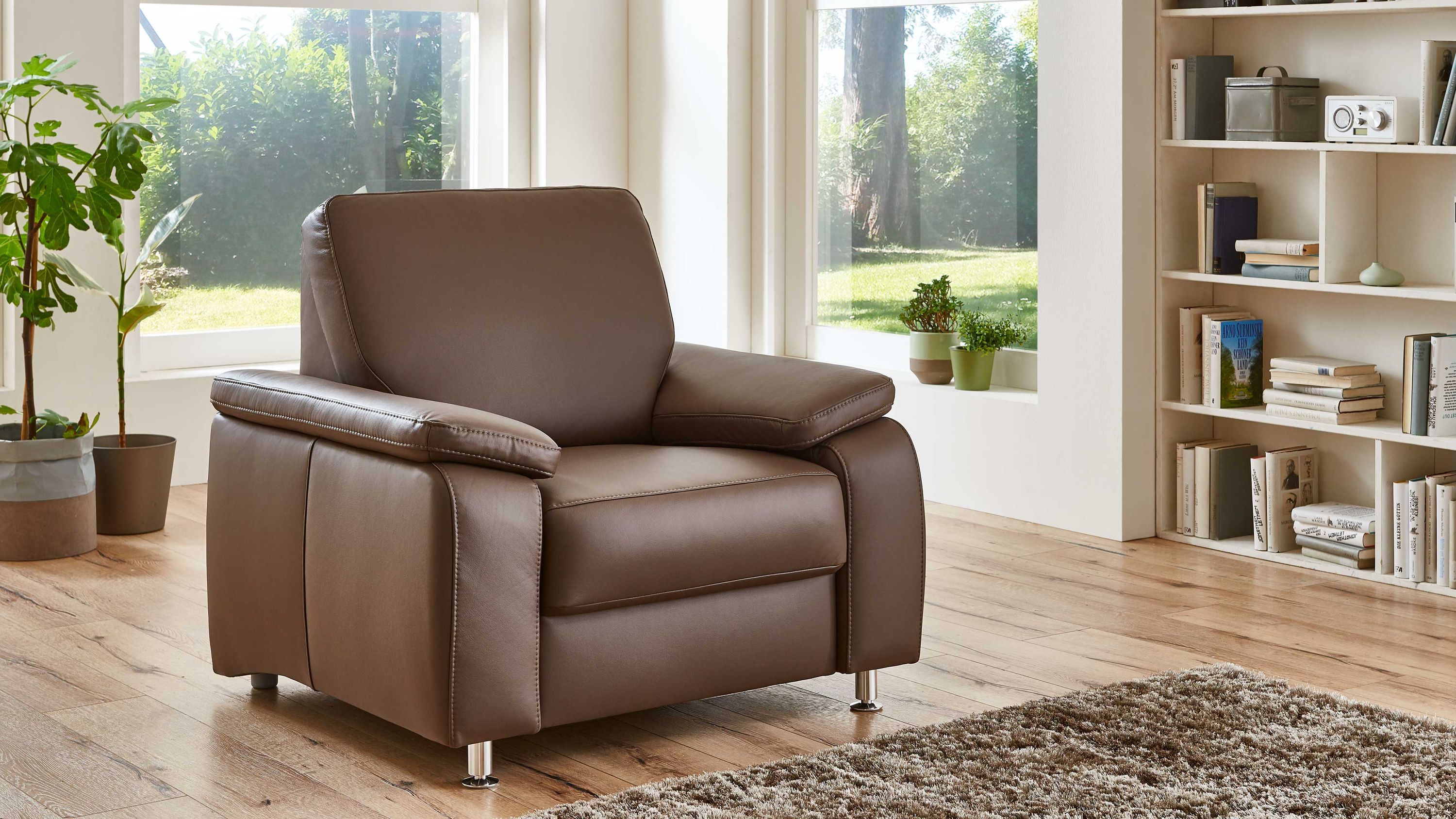 Polstersessel in moccafarbenem Leder mit Metallfüßen Polstersessel mit breiten Armlehnen und Metallfüßen in moccafarbenem Leder in hellem Wohnzimmer