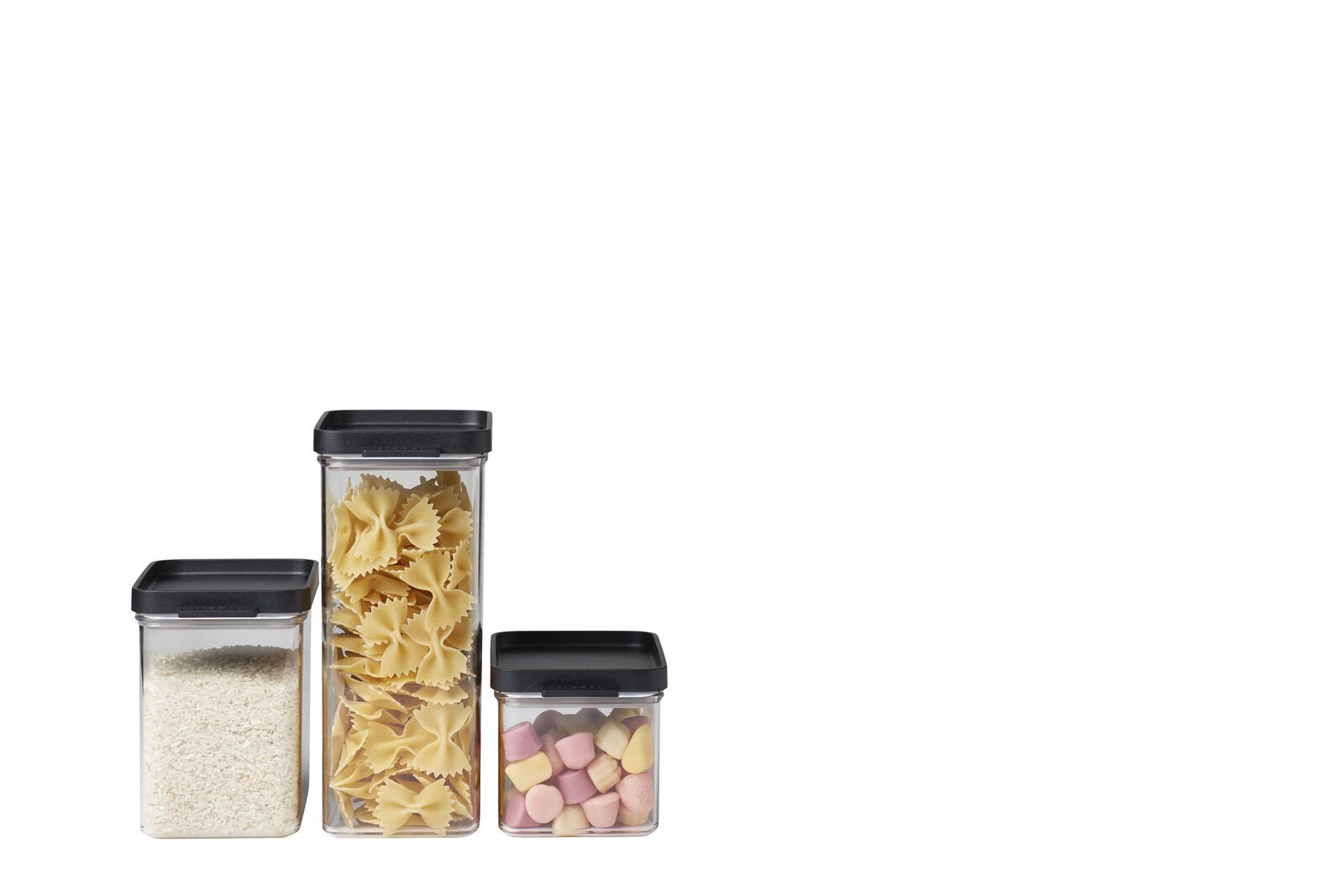 Drei transparente Dosen mit schwarzem Deckel, gefüllt mit Reis, Pasta und bunten Süßigkeiten, nebeneinander platziert