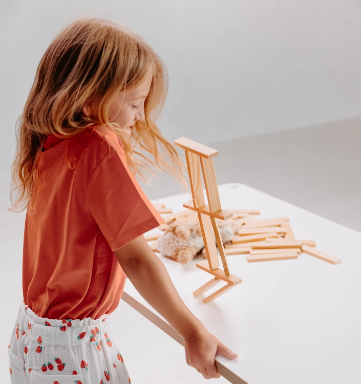 Mädchen poptop Kind spielt an weißem höhenverstellbarem Schreibtisch mit Holzbausteinen und Kuscheltier für kreatives Lernen und Freizeit.