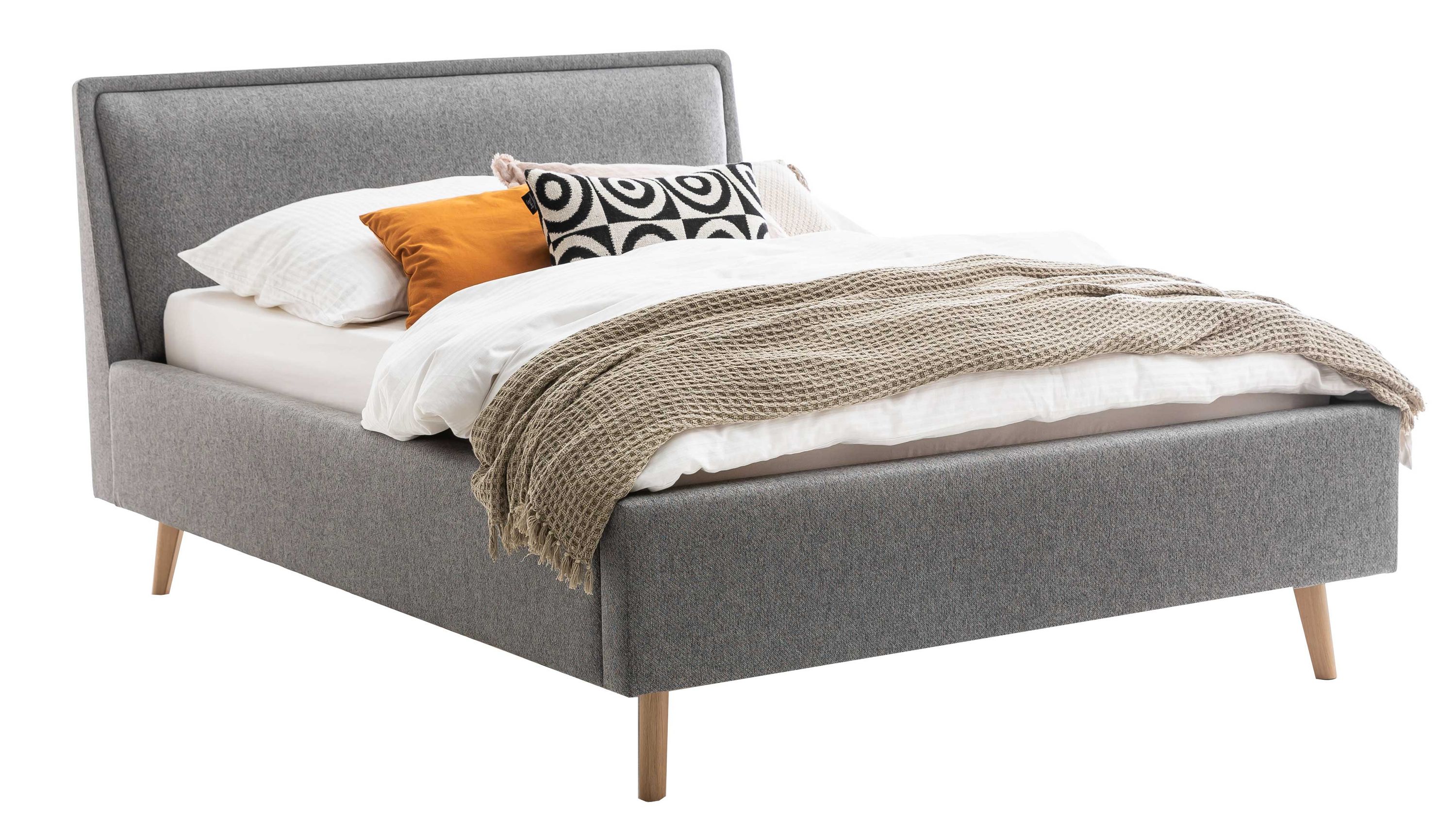 Polsterbett mit grauem Bezug und Holzfüßen Graues Polsterbett mit schrägem Kopfteil und hellen Holzfüßen mit Decke und Kissen belegt