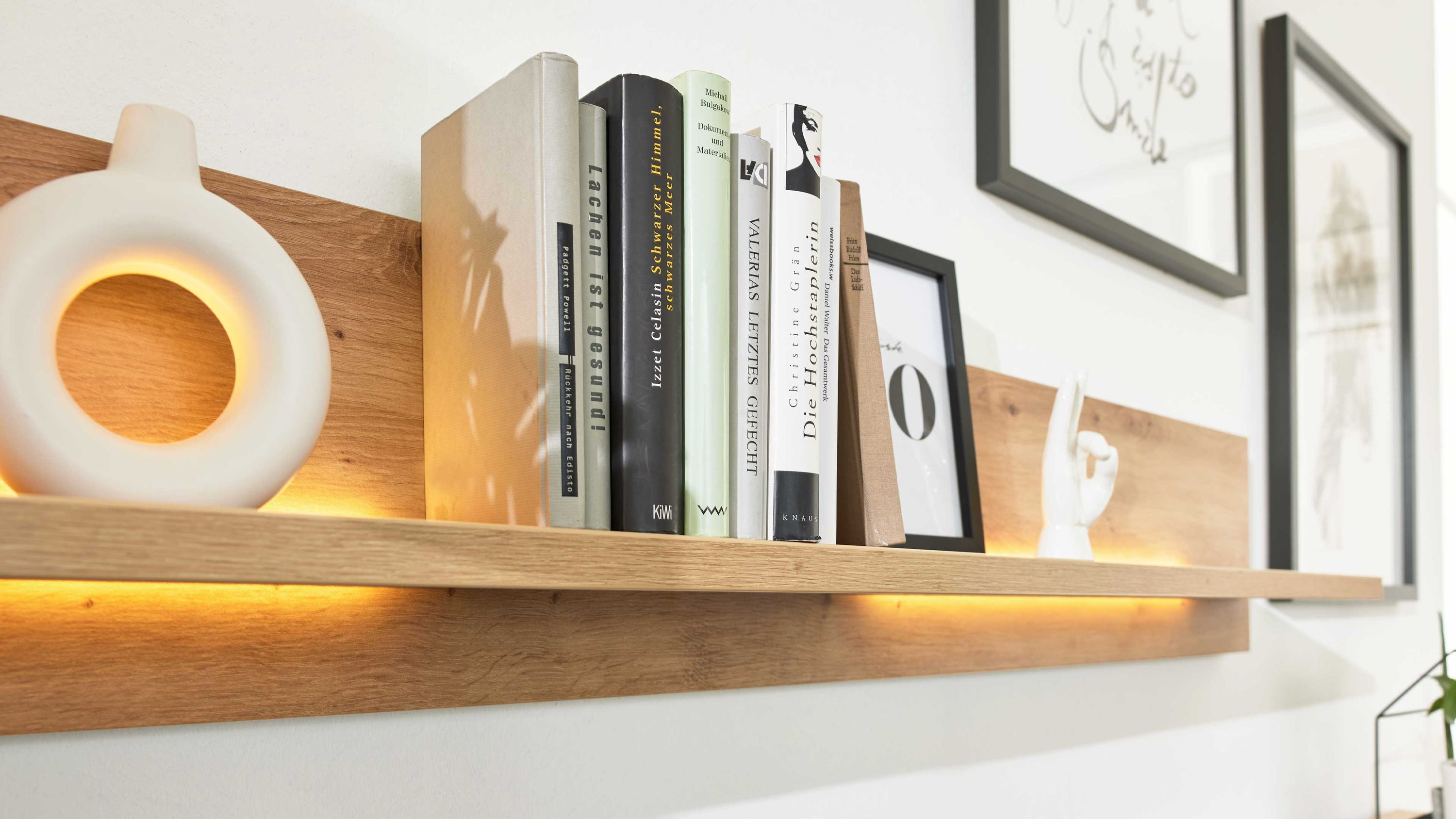 Holzregal mit integrierter gelber Lichtleiste darauf Bücher und Dekorationsobjekte