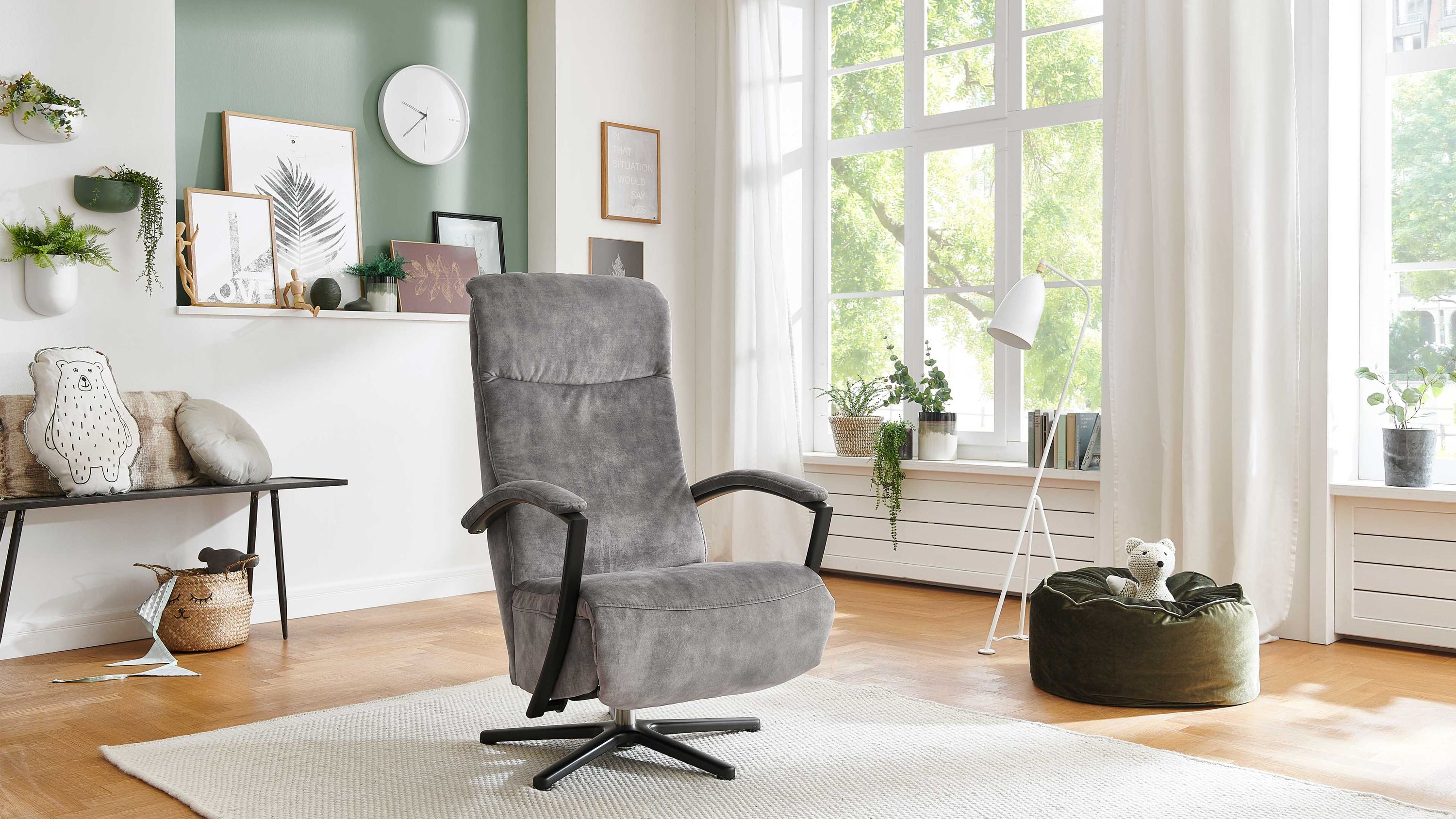 Grauer Relaxsessel mit Sternfuß Grauer Relaxsessel mit hoher Rückenlehne und schwarzem Sternfuß in hellem Wohnzimmer