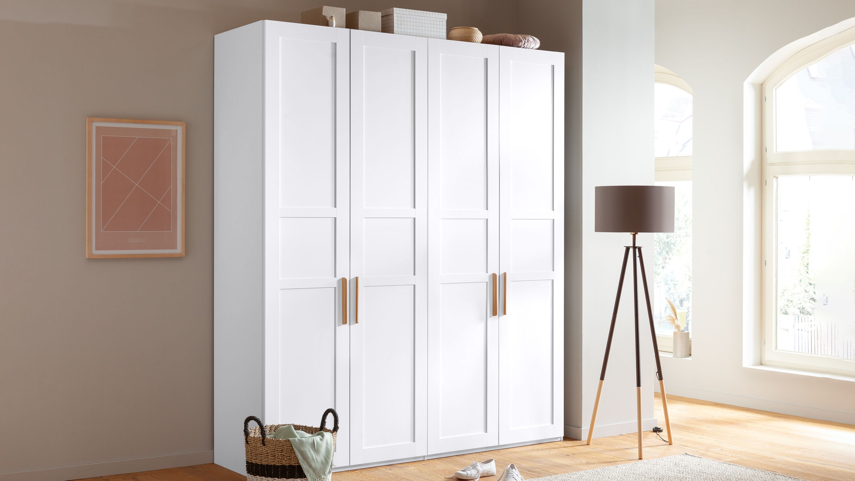 Viertüriger weißer Kleiderschrank mit Holzgriffen Viertüriger Kleiderschrank mit weißen Türen und Holzgriffen in hellem Raum mit Fenster und Stehlampe