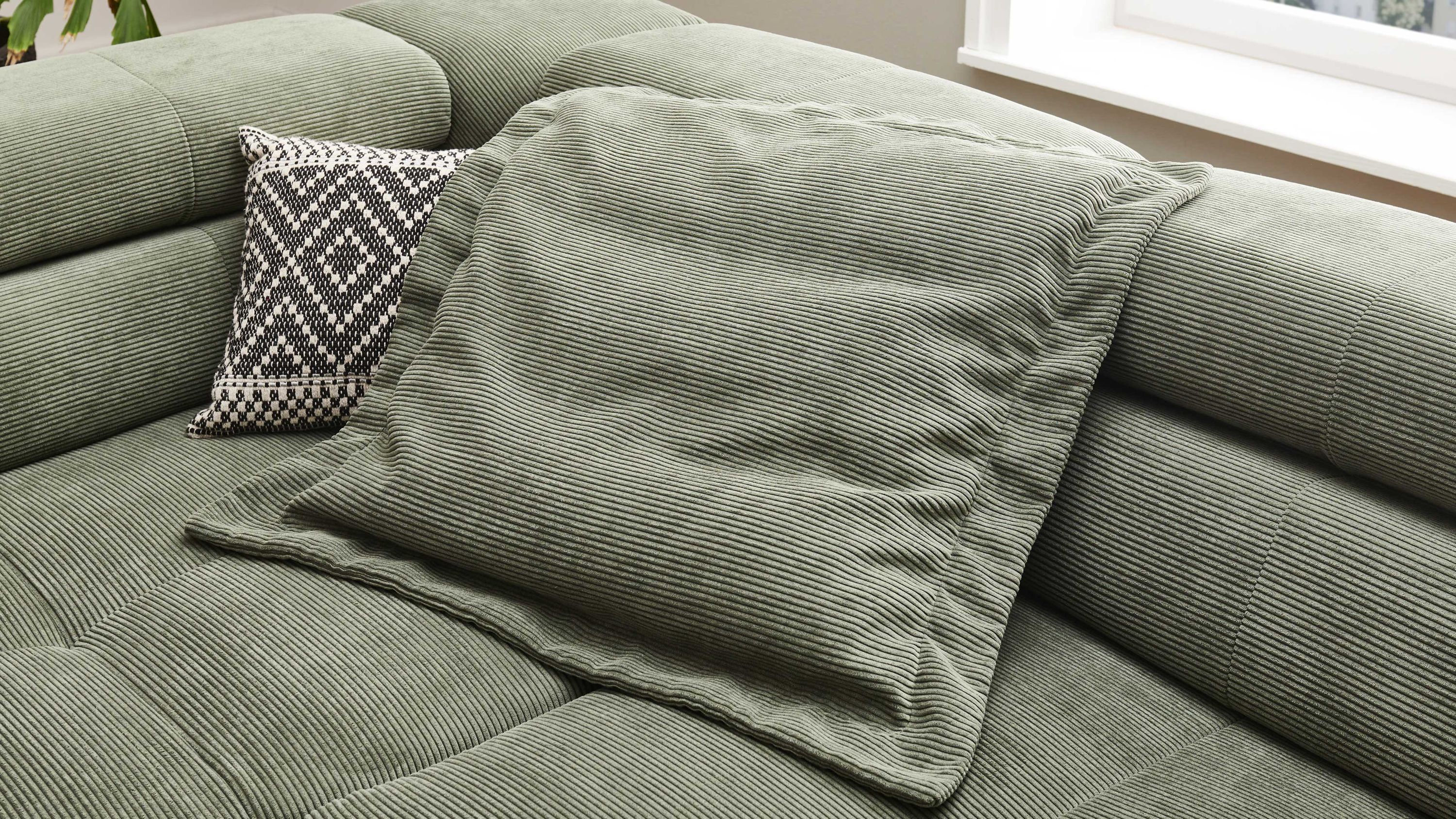 Grünes Kissen aus Feincord auf grünem Sofa mit Rautenmuster-Kissen im Hintergrund
