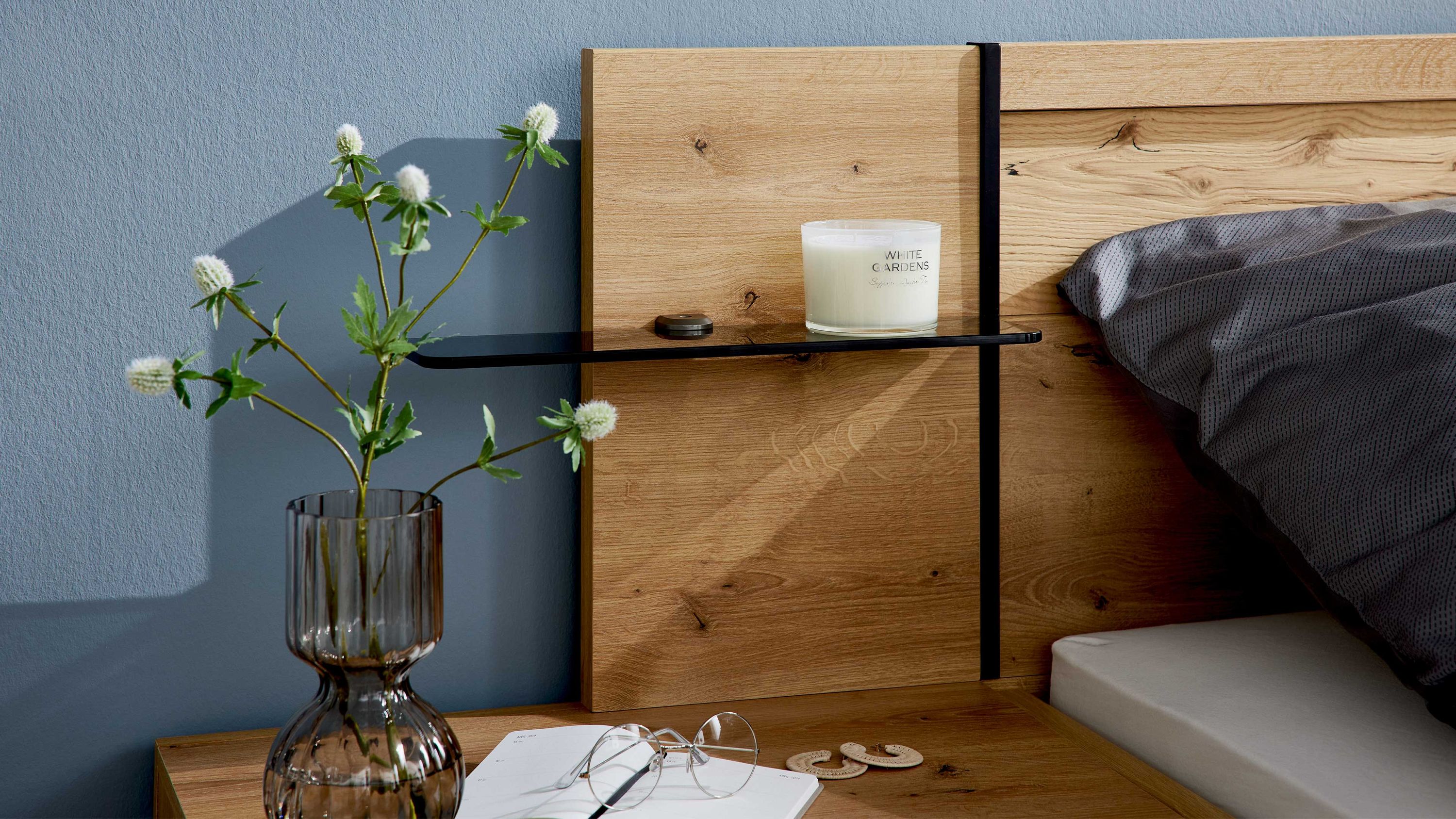 Zweiteiliges Paneel-Set aus Holz mit schwarzem Glasregal an einer blauen Wand neben einem Bett mit grauem Bettbezug