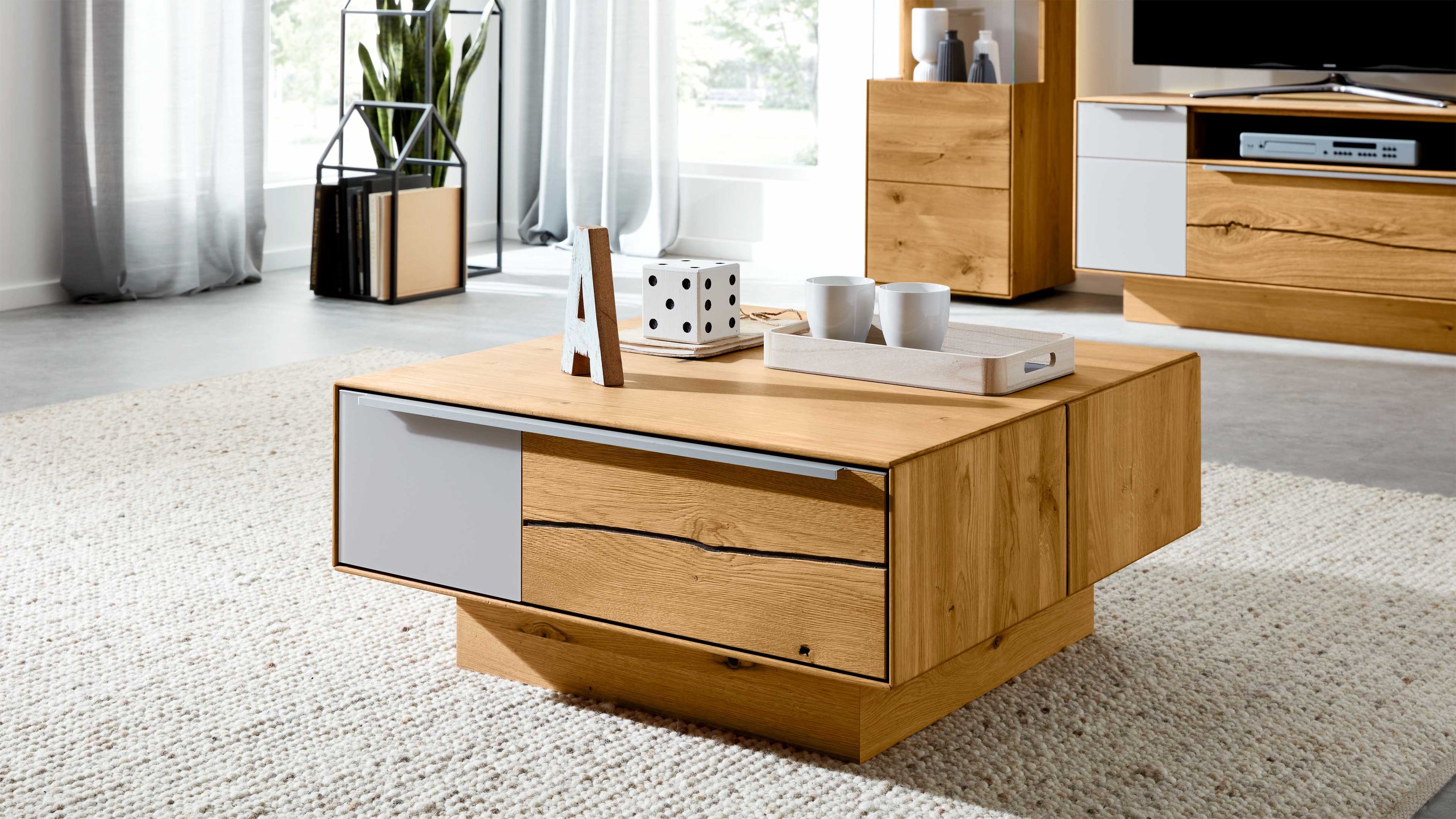 Quadratischer Couchtisch aus Holz mit zwei Schubladen und einer weißen Front auf hellem Teppich