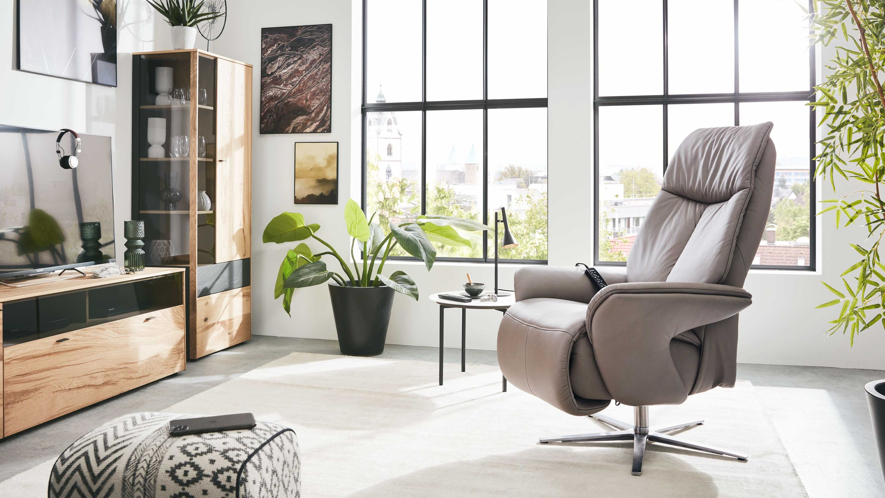 Sessel mit hoher Rückenlehne und gepolsterten Armlehnen in grauem Leder mit sternförmigem Metallfuß in modernem Wohnzimmer
